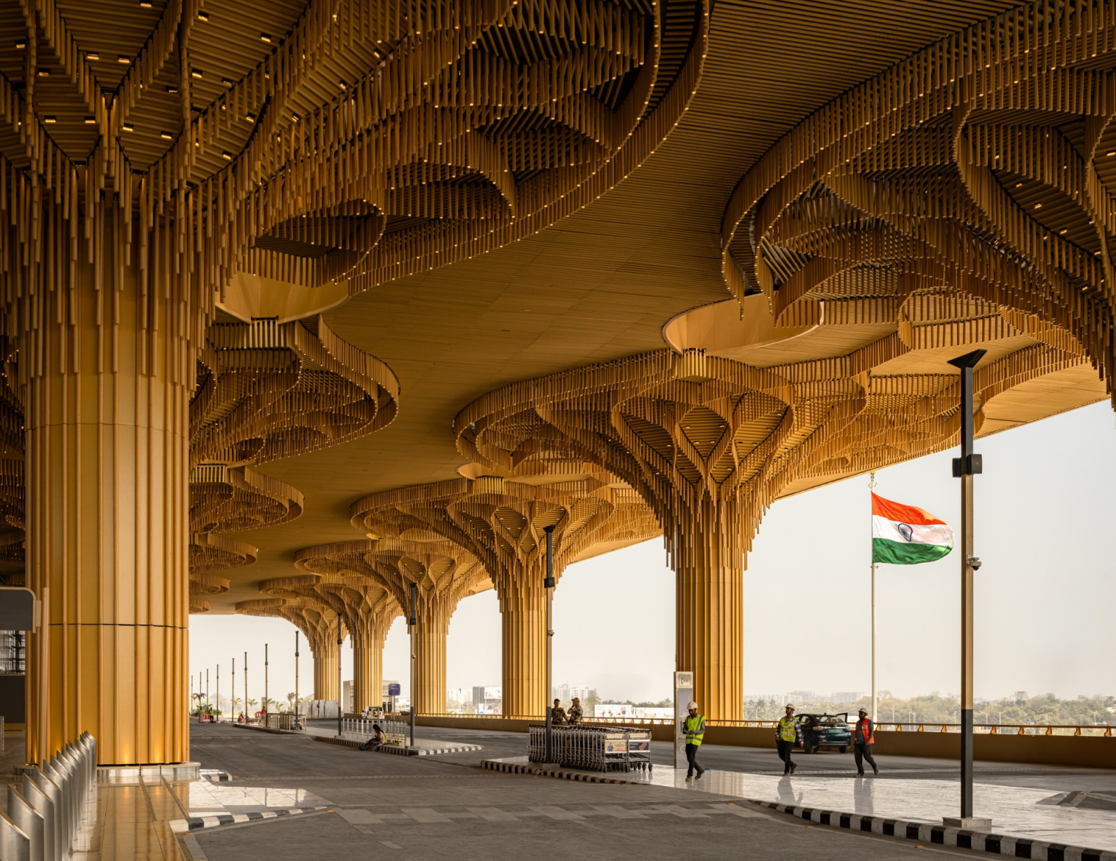 At the departures forecourt, a forest of golden timber-clad columns fans out into canopy-like brackets, framing views towards the city beyond