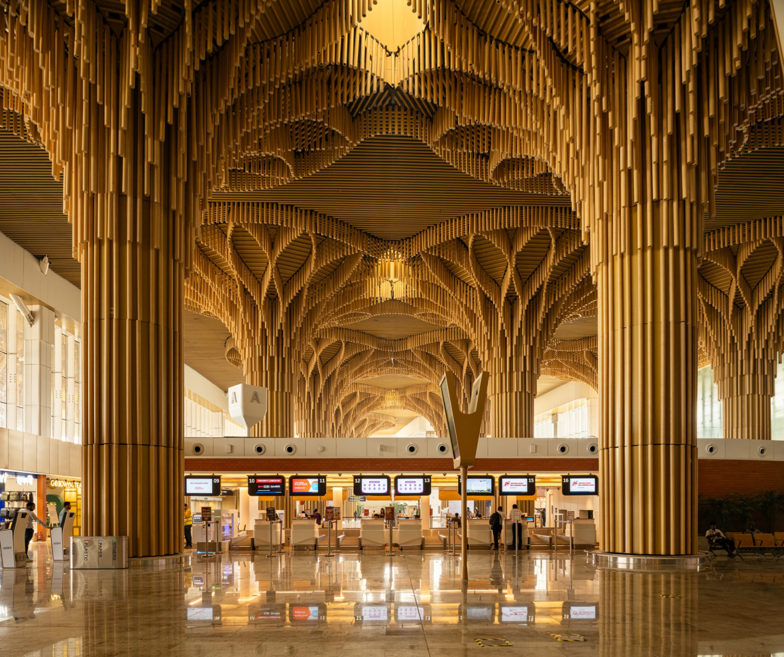 Inside the check-in hall, the tree-form canopies repeat in rhythmic succession, their interlaced timber fins creating a cathedral-like procession of light and shadow