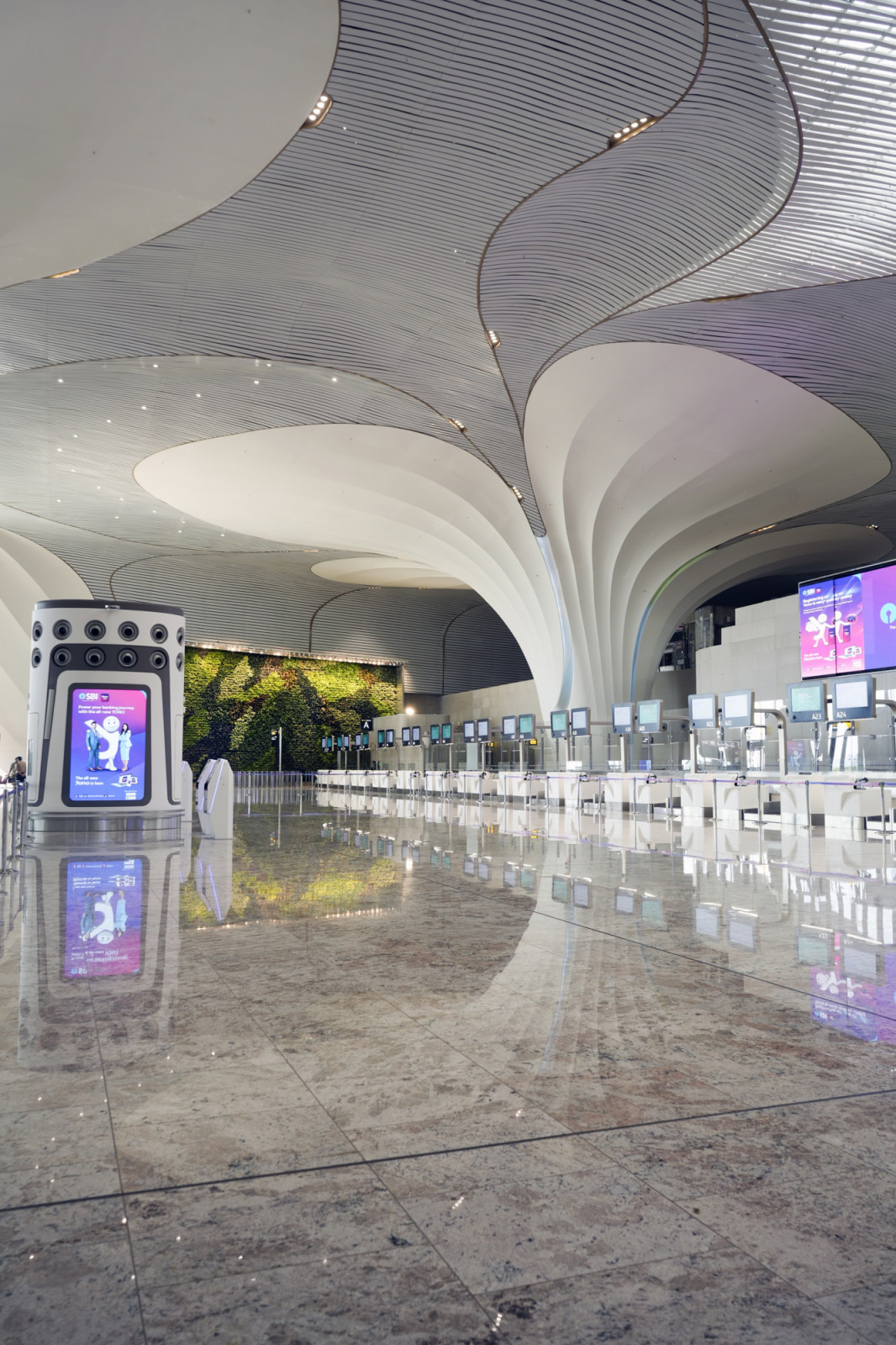 At the heart of the departures hall, the lotus columns flare outward into the ceiling’s petal geometry, with a living green wall marking one of the terminal’s digital art pause points.