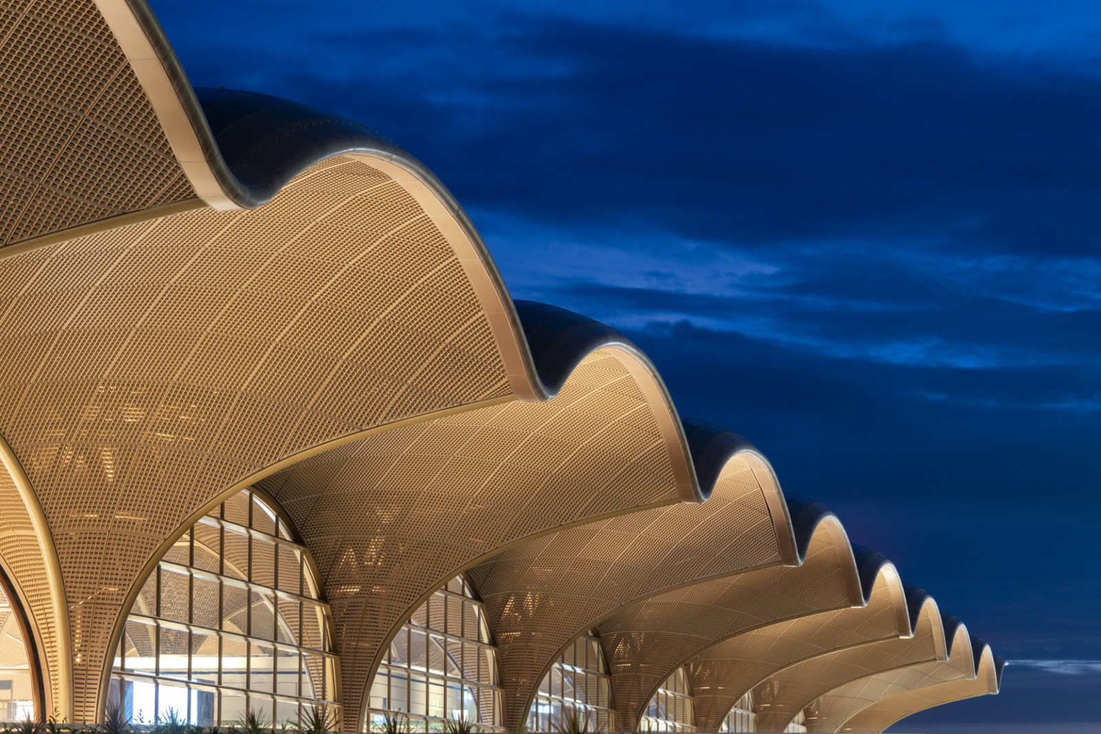 At dusk, the rippling sequence of woven roof vaults catches the last light, each scalloped form repeating along the terminal’s length against a darkening sky (Photo: Nigel Young)