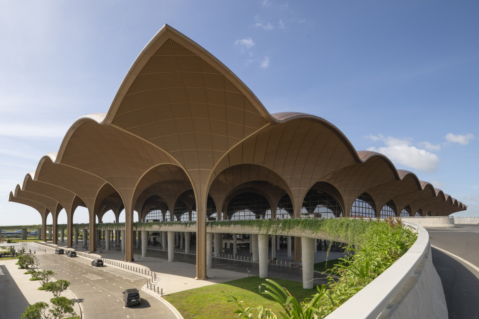 By day, the terminal’s undulating canopy reads as a procession of woven, leaf-like vaults, supported on slender columns above a planted green roofline (Photo: Nigel Young)