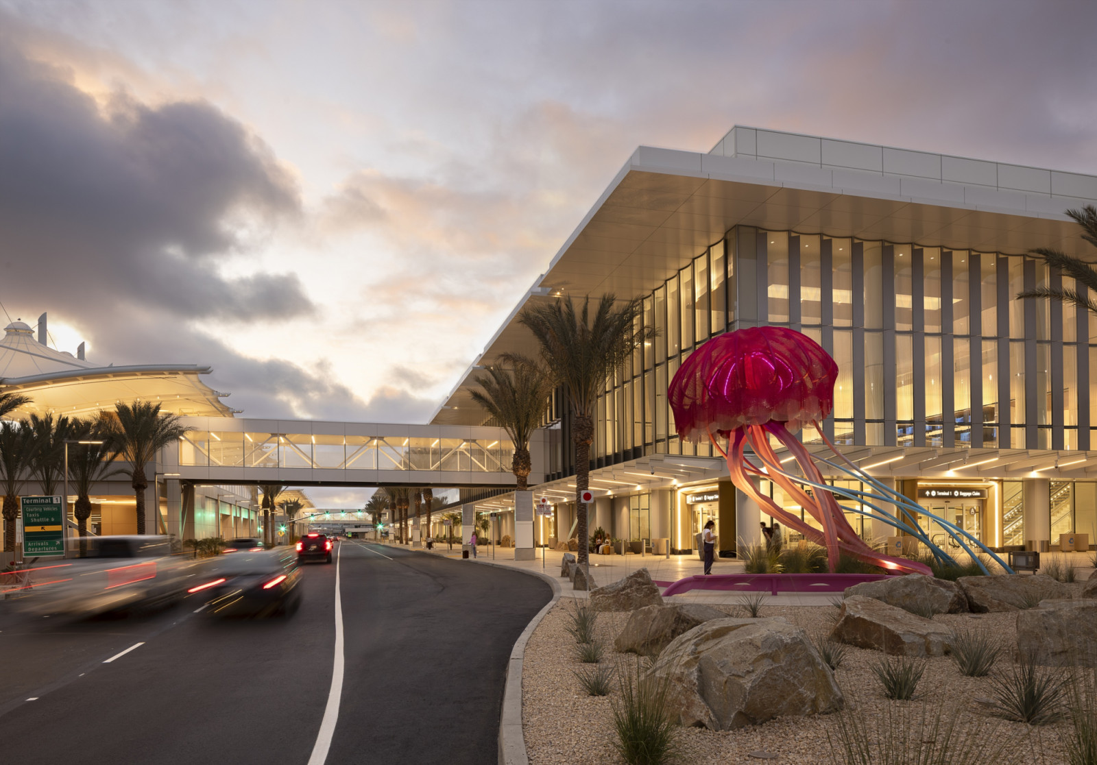 At dusk, a luminous pink jellyfish sculpture anchors the kerbside approach, set against the terminal’s cantilevered roofline and connecting skybridge (Photo: Ema Peter)