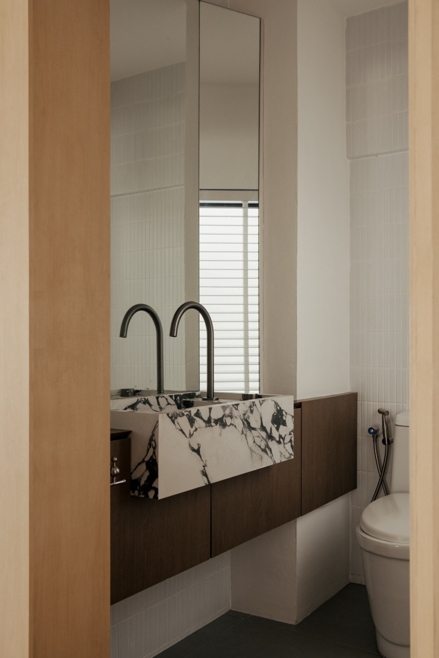 A guest bathroom with a marble double-basin vanity on a walnut-toned cabinet, black curved taps, a full-height mirror, and small-format white wall tiles