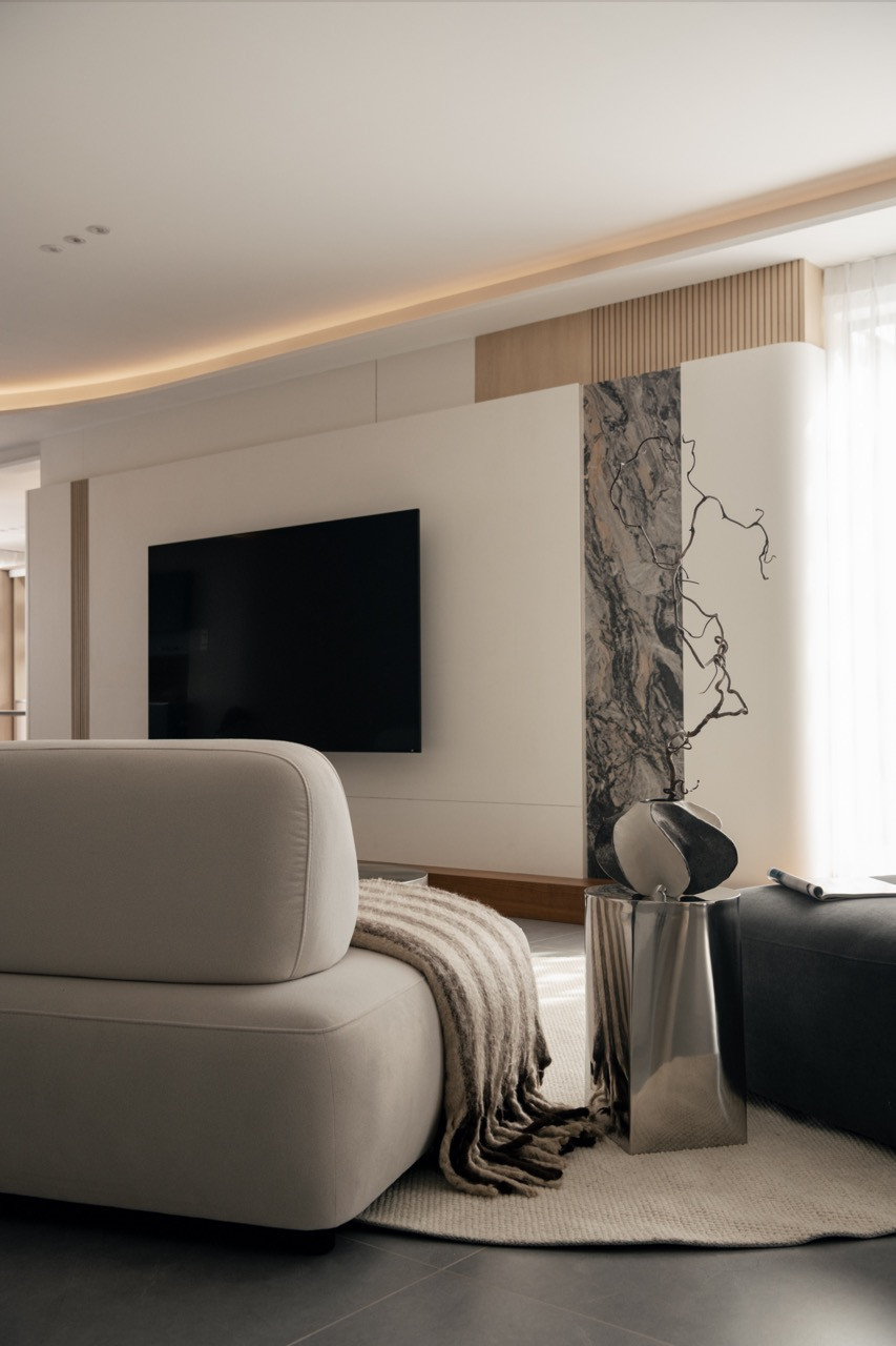 The living area with cream modular sofa, Arabescato Orobico marble feature panel, sculptural side table and dried branch arrangement, with the layered curved ceiling above