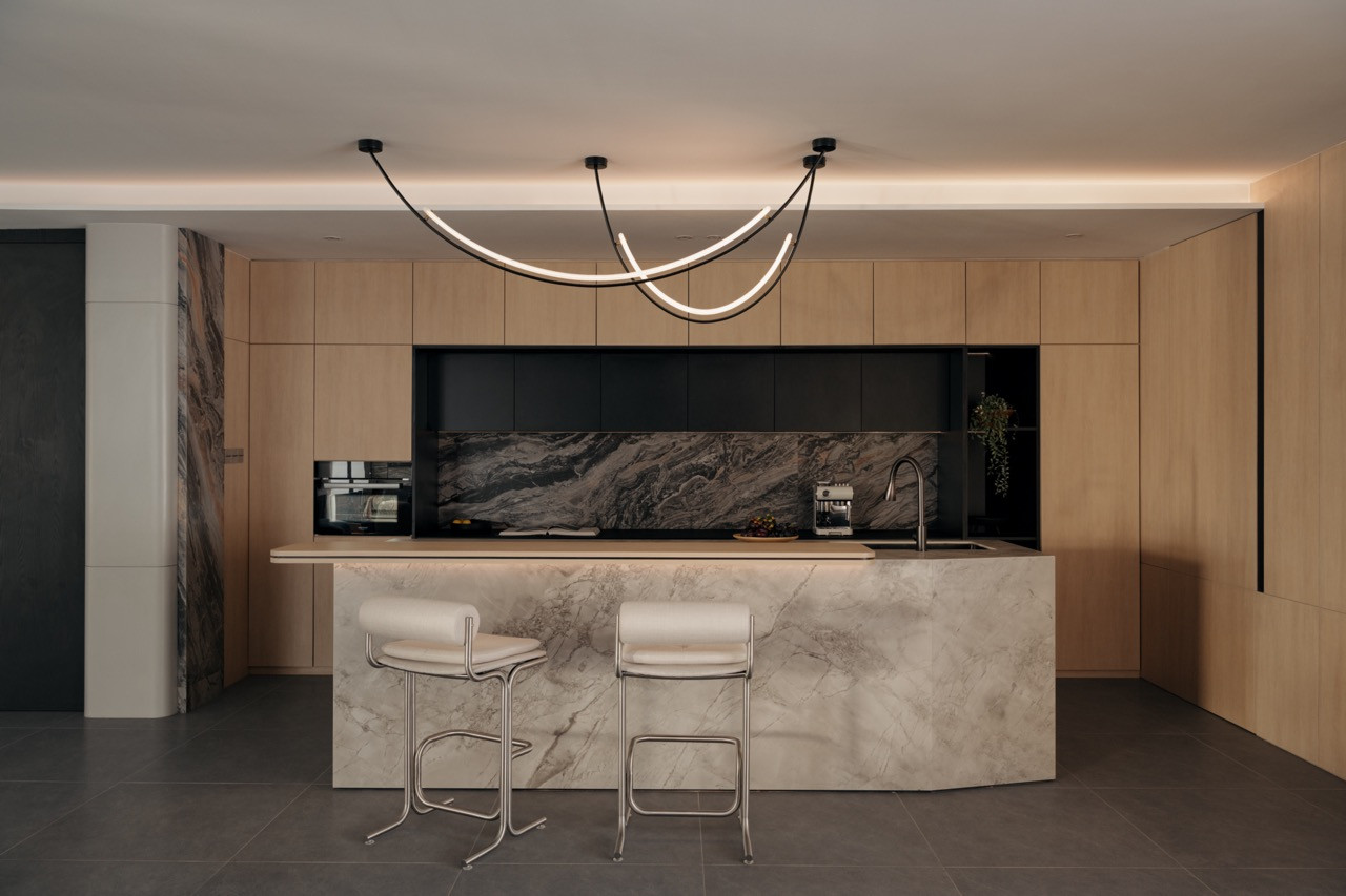 The kitchen island in Bianco Carrara marble with bar stools and looped pendant light, set against the Arabescato Orobico marble splashback and oak-toned upper cabinetry