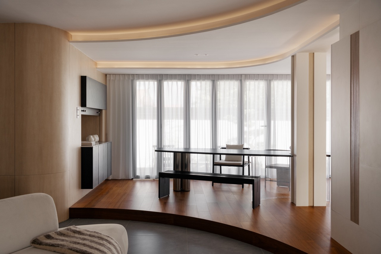 The curved teak timber platform delineates the dining area from the living space, with the corresponding curved ceiling above and large folding doors opening to the garden beyond