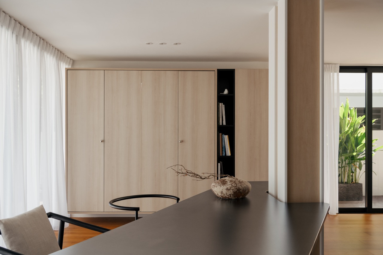 View from the dining table towards the oak-toned storage wall with an open bookshelf unit, with garden greenery visible through the sliding doors to the right