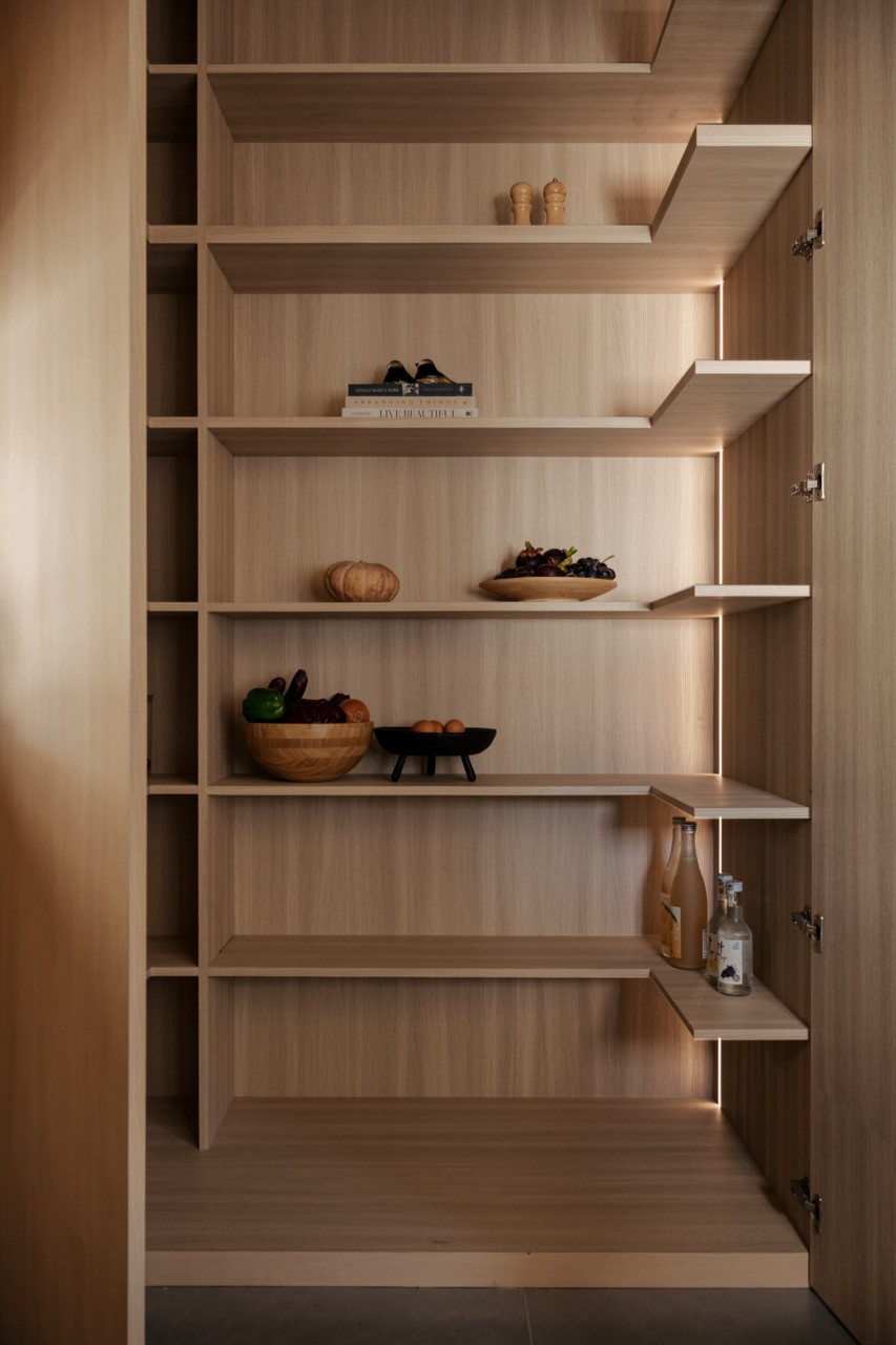 Open oak-toned pantry shelving in the kitchen area, displaying produce, cookbooks, and ceramics