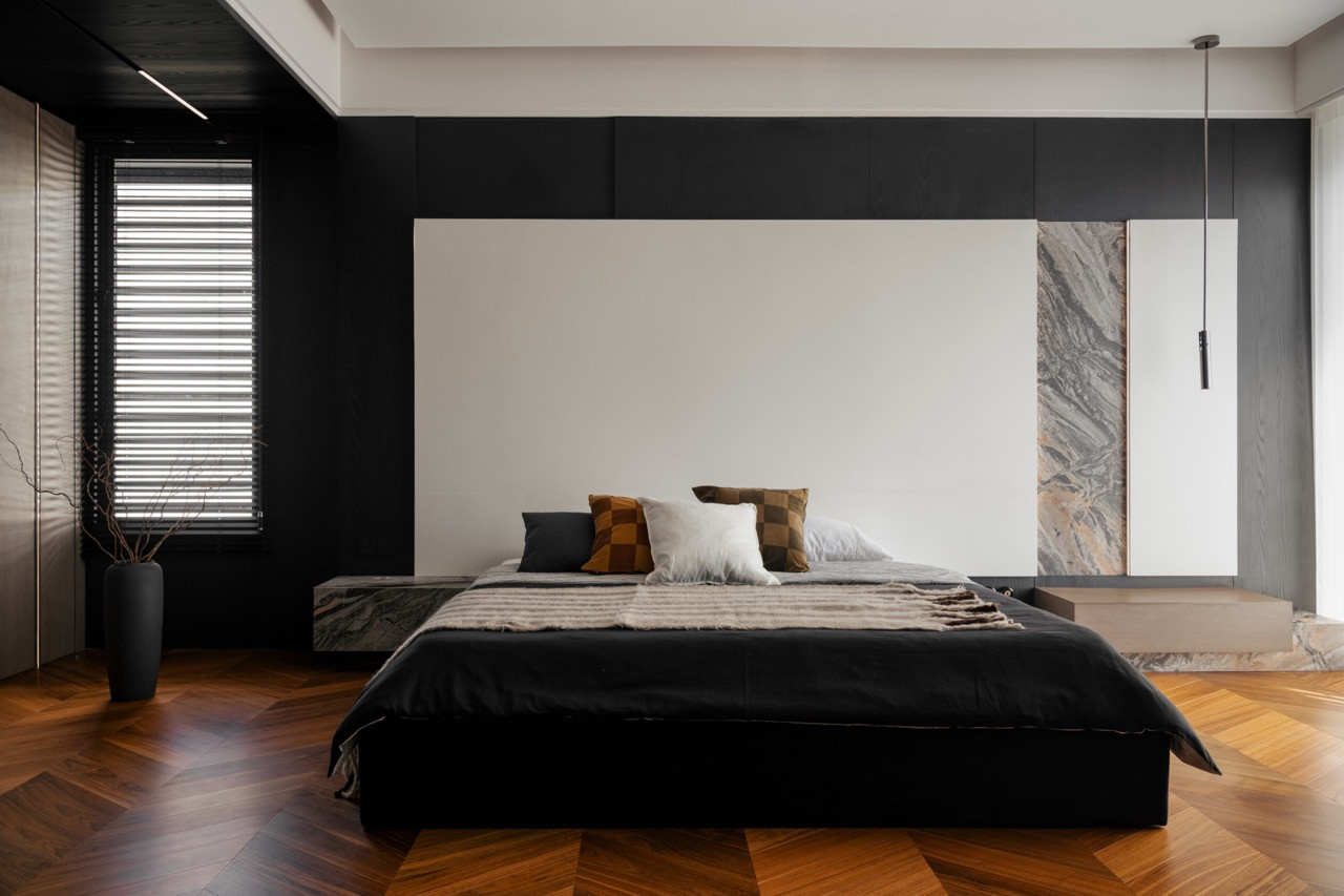 The master bedroom with a low-profile black bed, teak herringbone flooring, Arabescato Orobico marble feature panel, and a slim pendant light