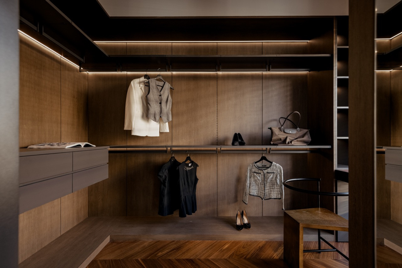 The walk-in wardrobe with full-height oak-toned cabinetry, open hanging rails, integrated lighting, and a teak herringbone floor