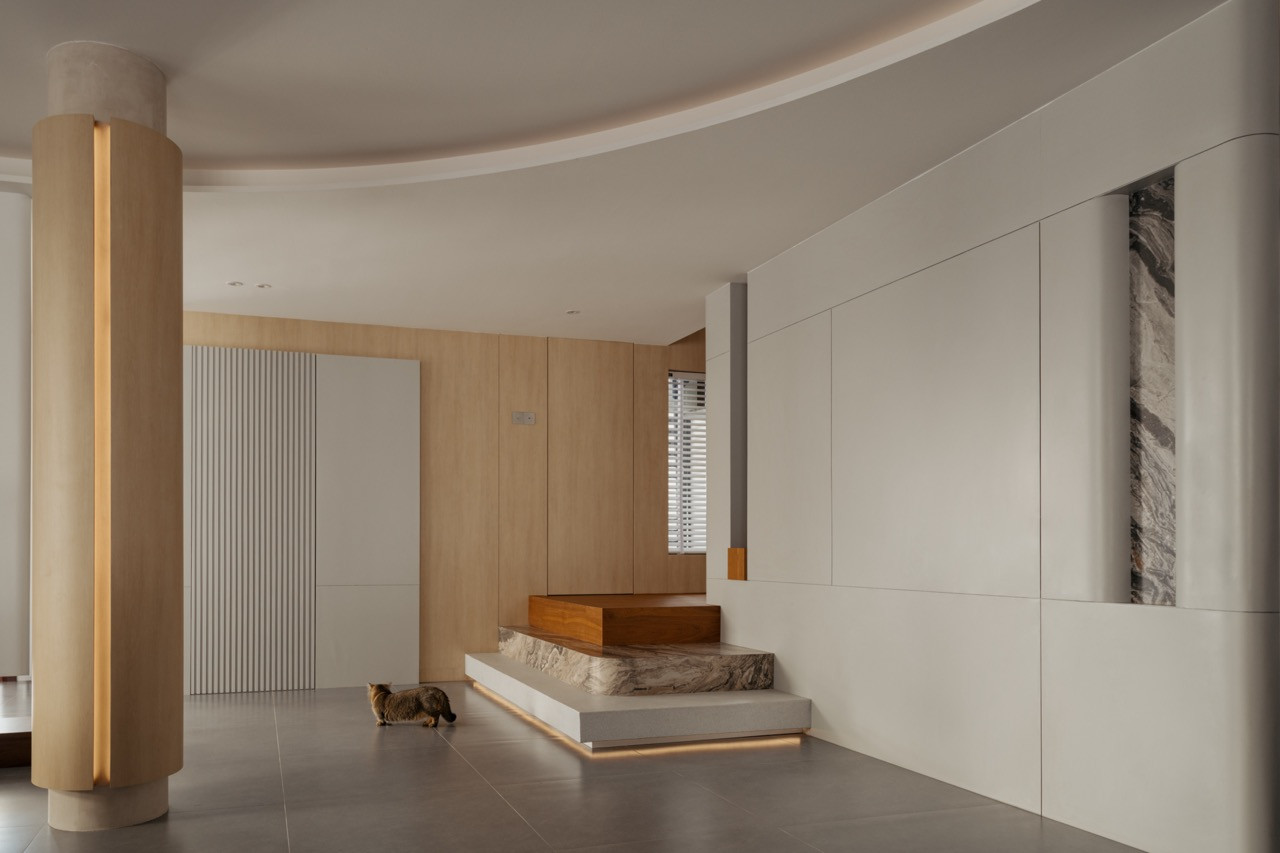 View of the entrance foyer with curved ceiling, illuminated column, three-step staircase, fluted wall panel, and Arabescato Orobico marble feature inset; the family cat walks across the ground floor