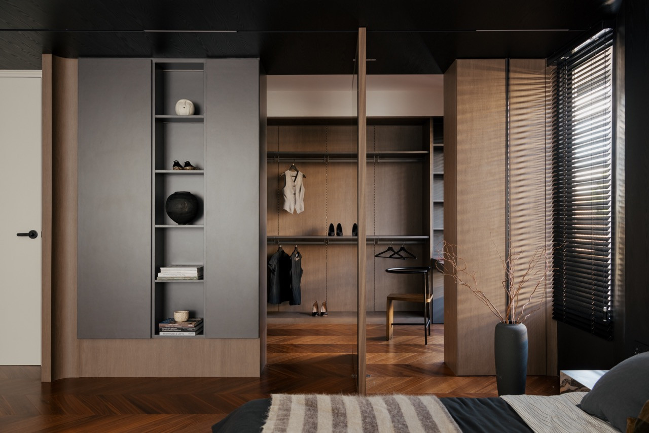 The master bedroom storage wall with sliding wardrobe doors open to reveal the walk-in wardrobe beyond, finished in contrasting grey and oak tones