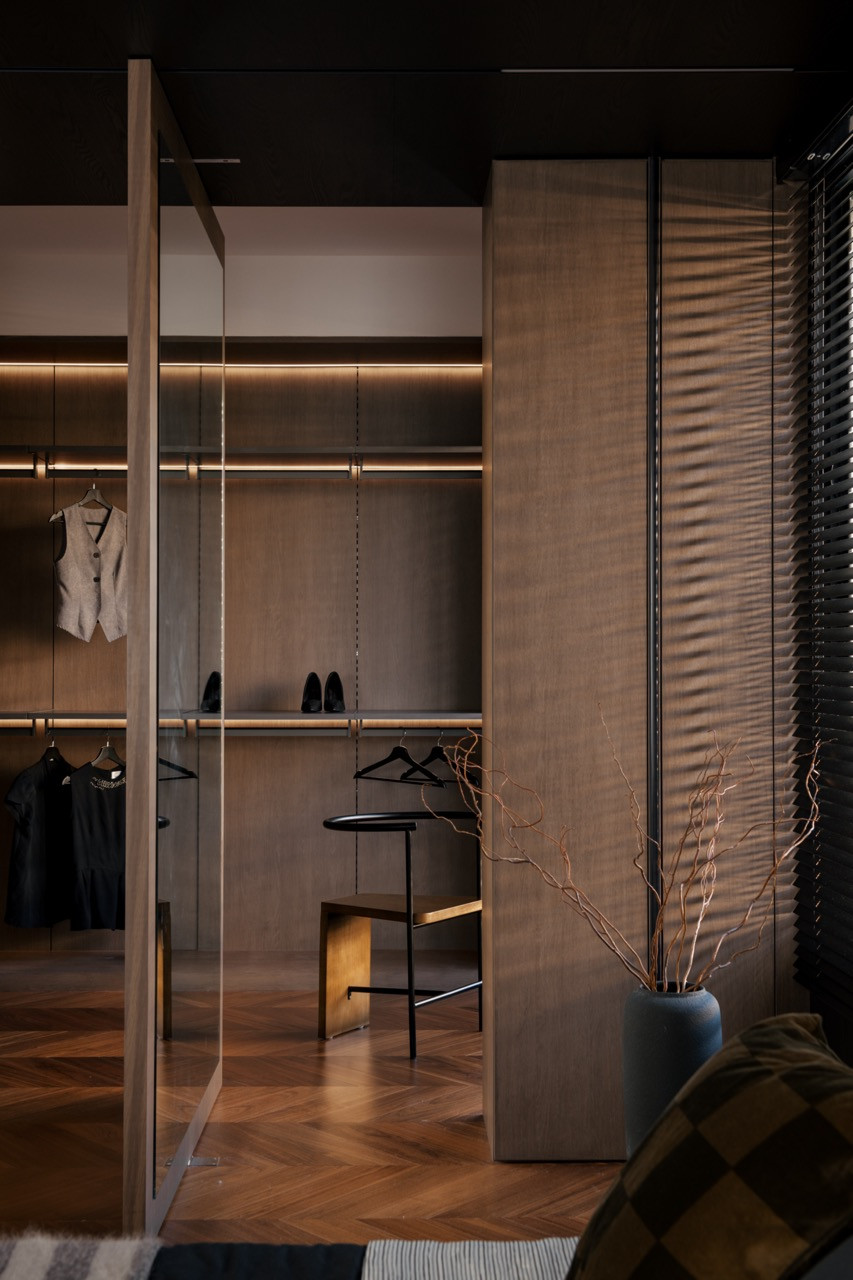 View into the walk-in wardrobe through the glazed partition, with oak-toned cabinetry, open hanging rails, and a black metal stool