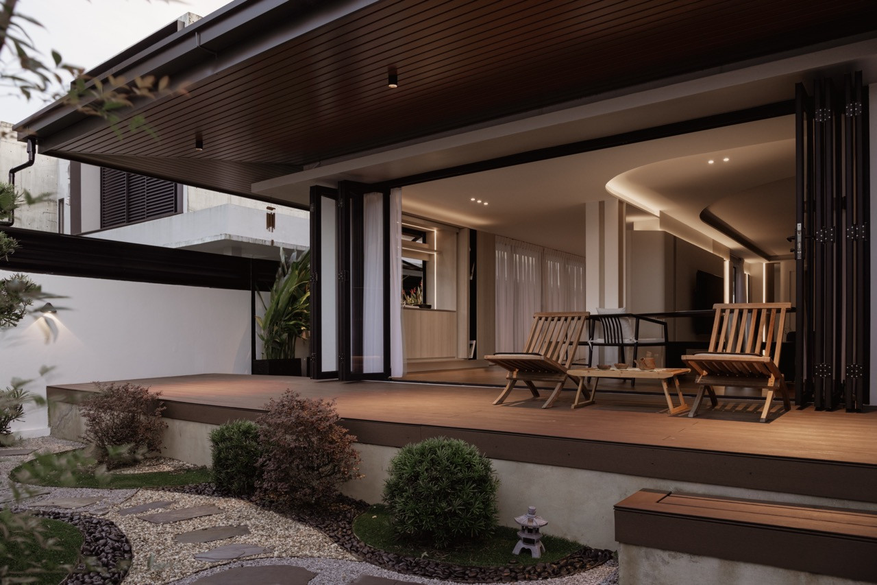 View from the backyard garden into the dining and living areas at dusk, with the large folding doors fully open, curved ceiling and strip lighting visible inside, and landscaped garden with stepping stones in the foreground