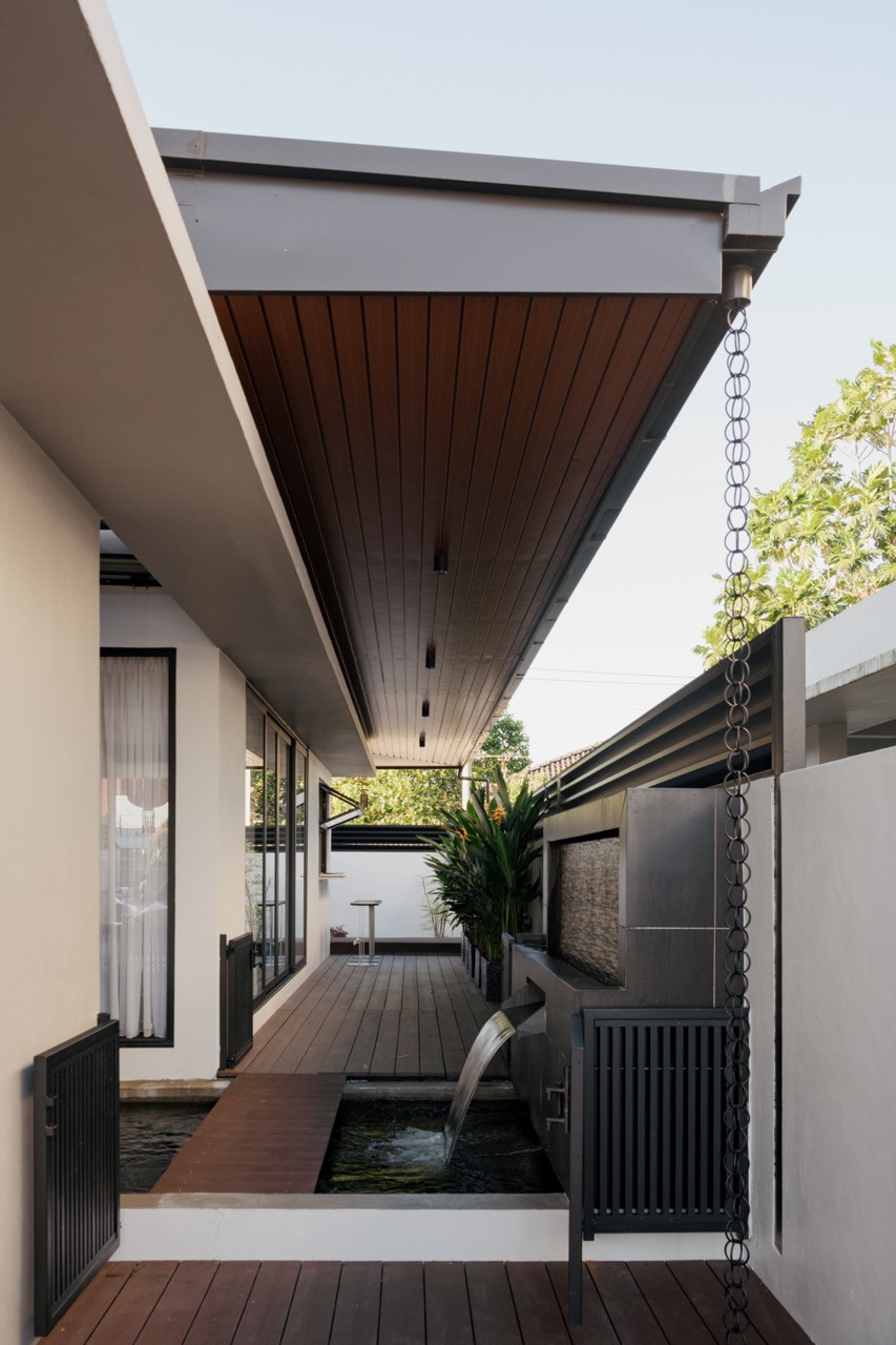 The side garden with a solar-powered fish pond, timber deck, water feature spout, chain rain drainage, and slatted timber ceiling along the covered walkway