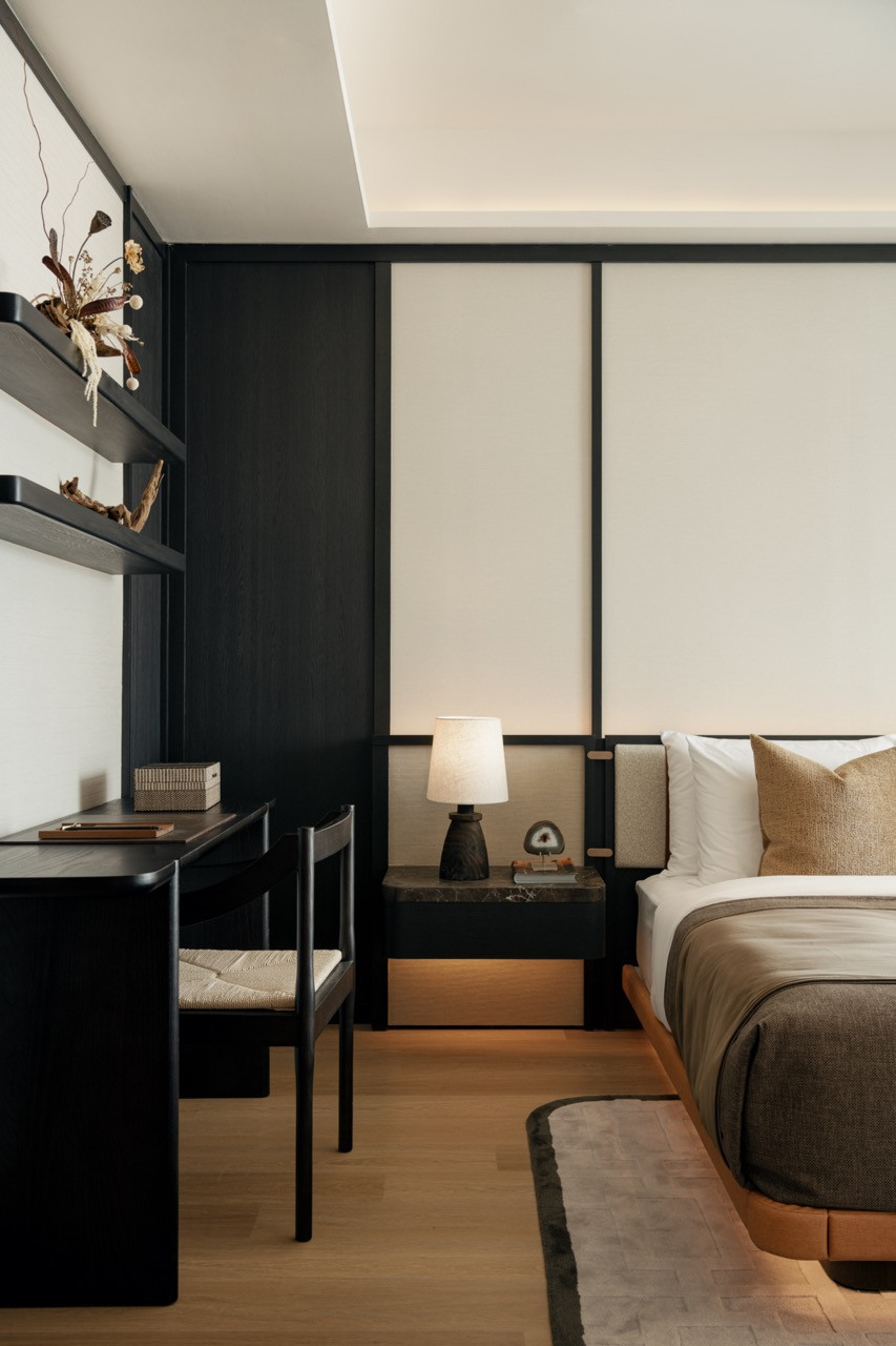 The master bedroom of the Type M unit, where ebonised joinery and upholstered wall panels set a considered contrast against warm timber flooring