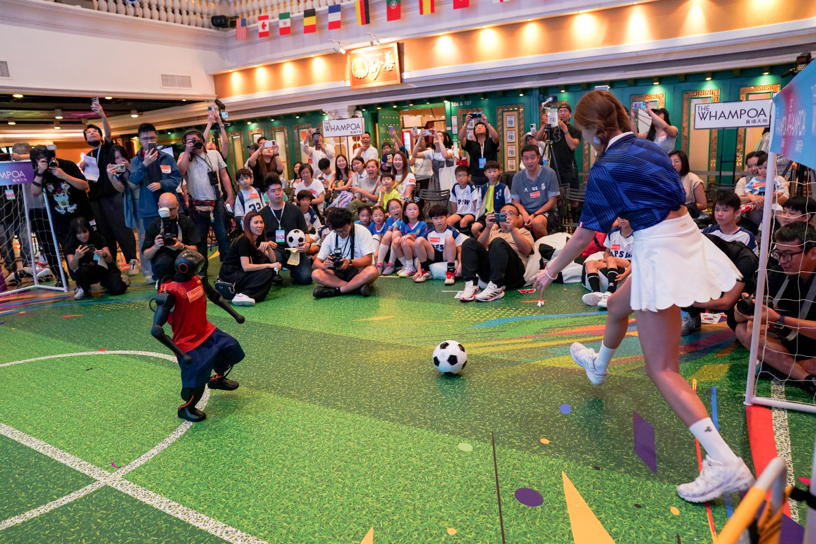 A girl plays soccer with a humanoid robot at Whampoa shopping complex on June 12, 2026 in Hong Kong, China. The Whampoa shopping complex kicked off its livestream of the 2026 FIFA World Cup on June 12 with a Robo Cup event. Kids aged 6 to 12 years old can join in the fun by playing football with artificial intelligence-powered soccer robots. (Photo by Zhang Xiangyi/China News Service/VCG via Getty Images)