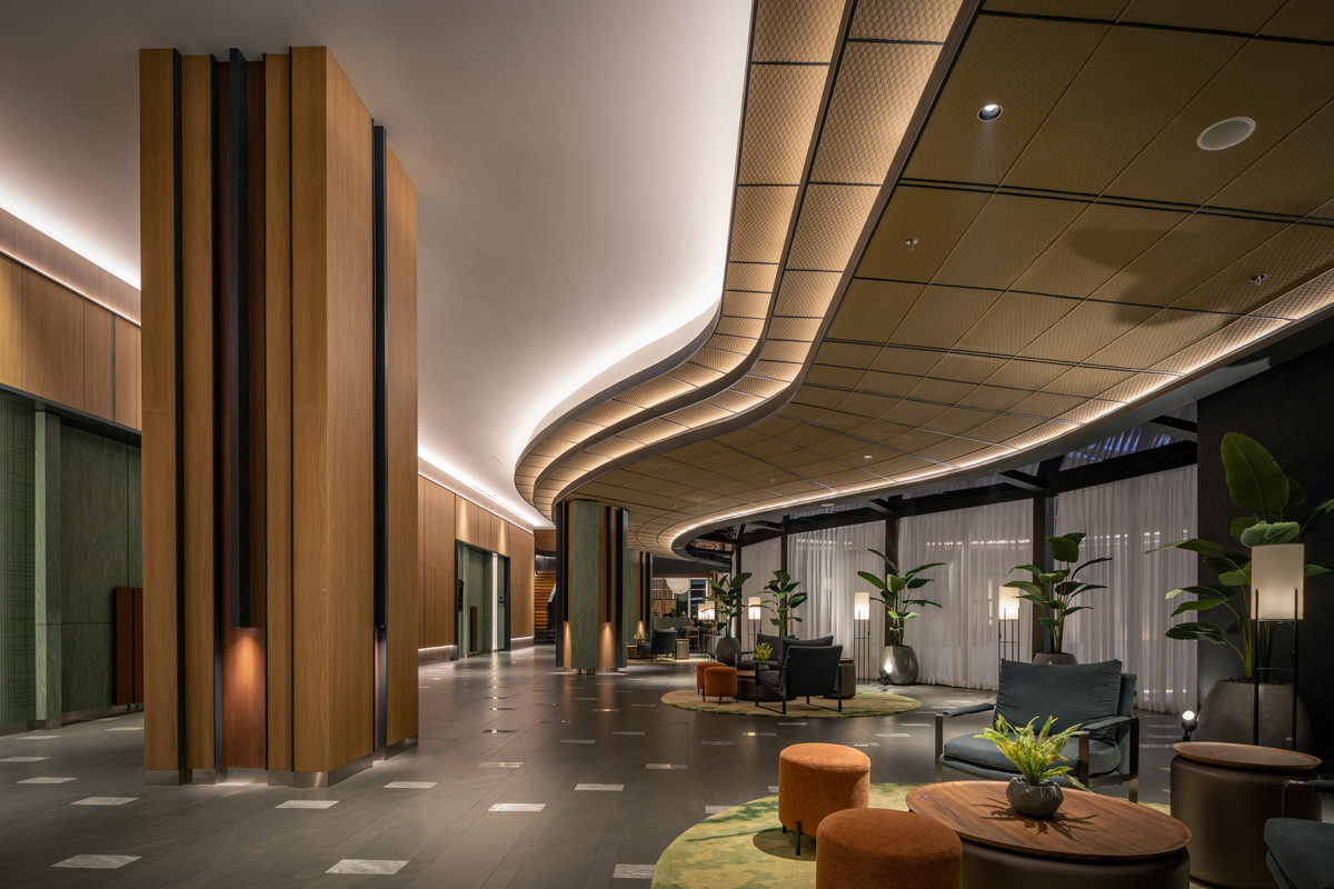 The lobby corridor of the Artotel Living World Grand Wisata in Bekasi, Indonesia, makes an immediate impression with its undulating illuminated ceiling and warm timber columns, a project realised by KCS (Karya Citra Simetri), Mark Associates, and ARTG Design Indonesia