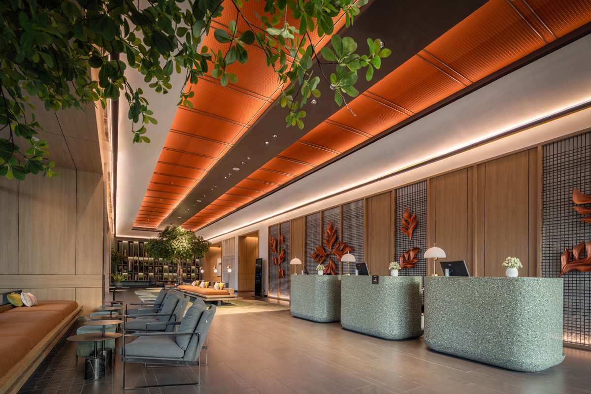 Terrazzo reception counters, hand-sculpted botanical wall reliefs, and a vivid orange ceiling define the arrival experience at the Artotel Living World Grand Wisata, realised by KCS, Mark Associates, and ARTG Design Indonesia
