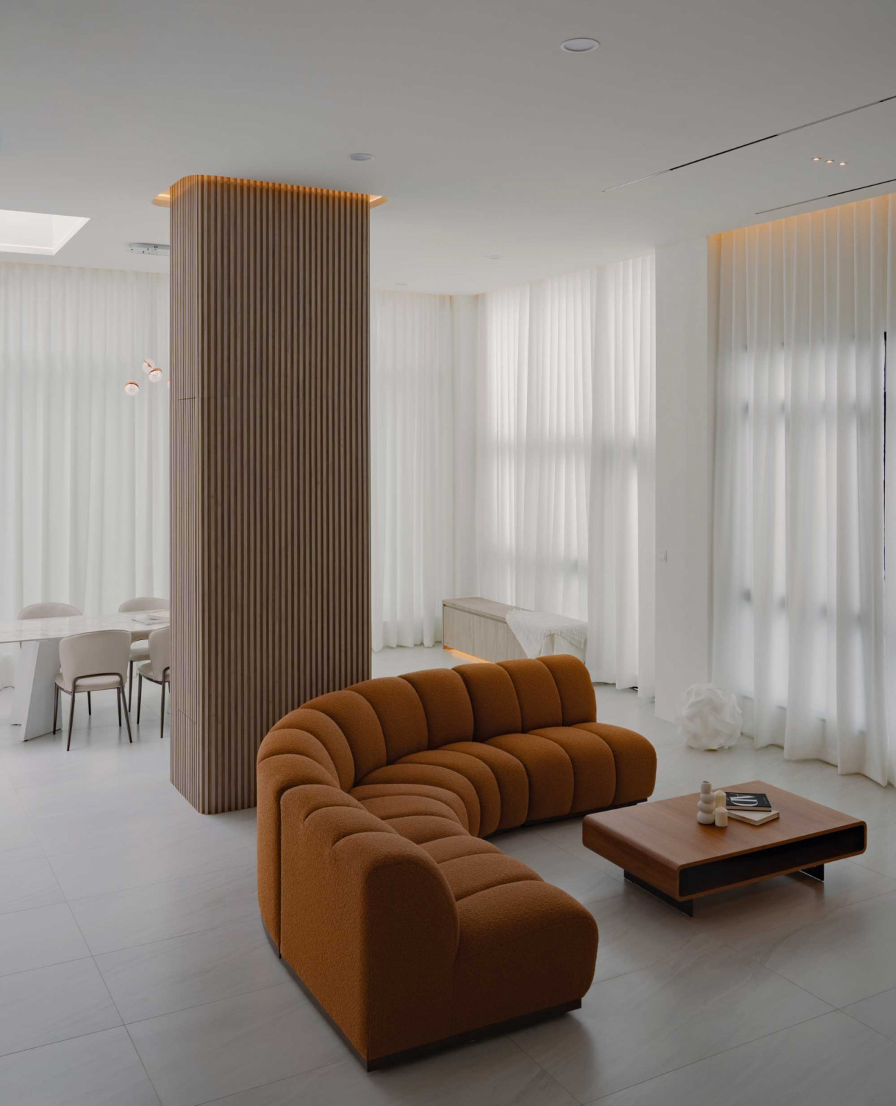A curved sofa anchors the living area, framed by sheer curtains and a fluted timber column that defines zones within the open plan