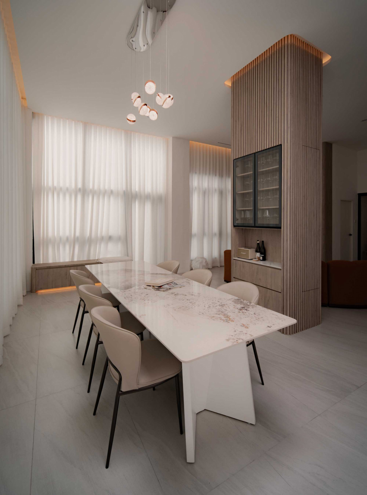 The dining area is centred on a marble table, with the fluted timber volume integrating storage while maintaining visual continuity