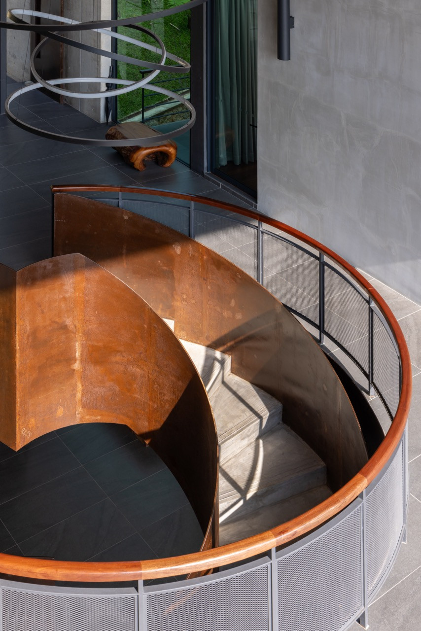 The curved staircase, viewed from above, where steel plates were used as permanent formwork, oxidised over time, leaving a mottled, rust-toned surface on the sinuous structure