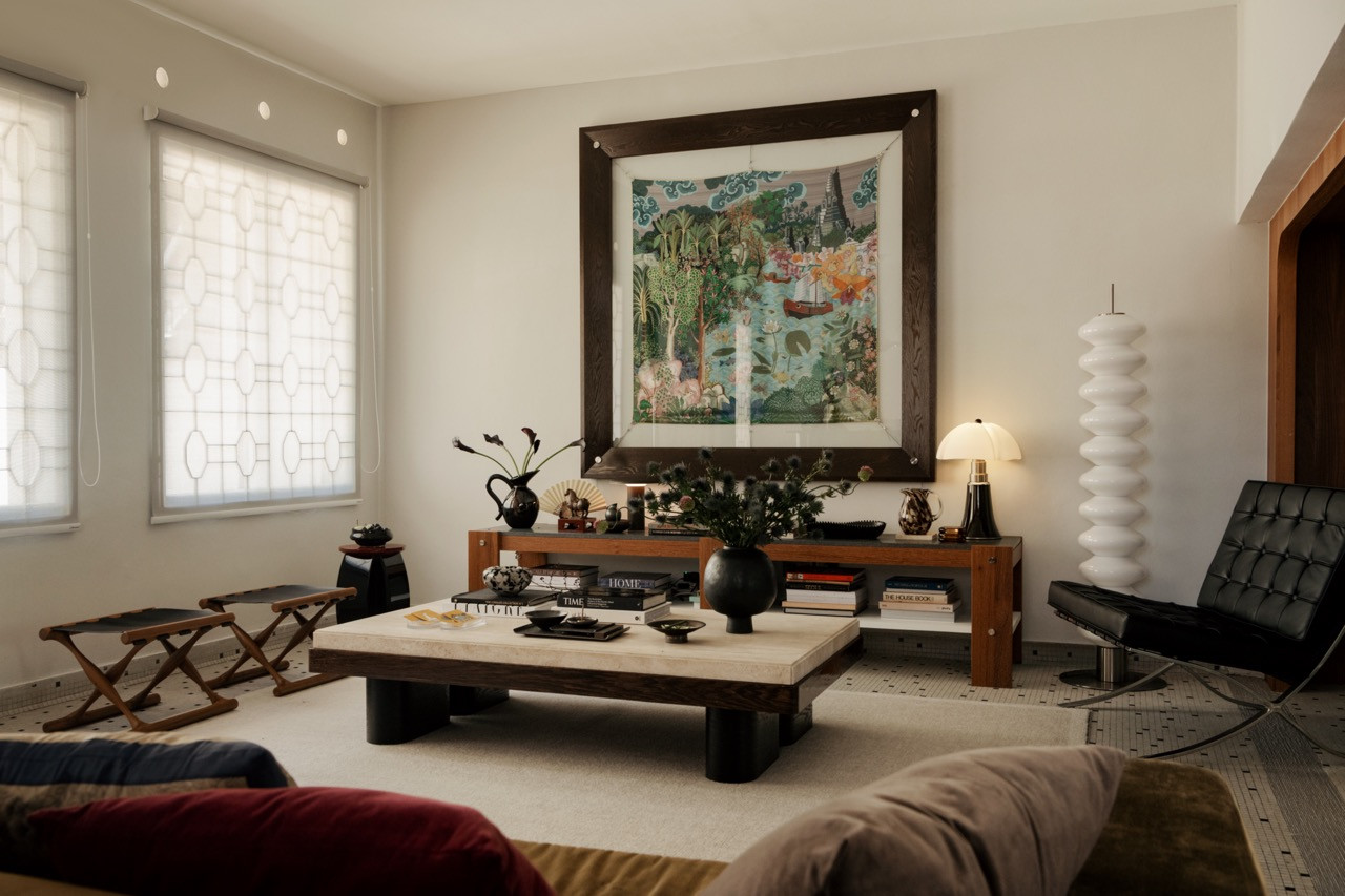 The reception room in full: the large tropical garden tapestry anchors the far wall above the console, with the travertine coffee table, Barcelona chair and stacked ceramic floor lamp