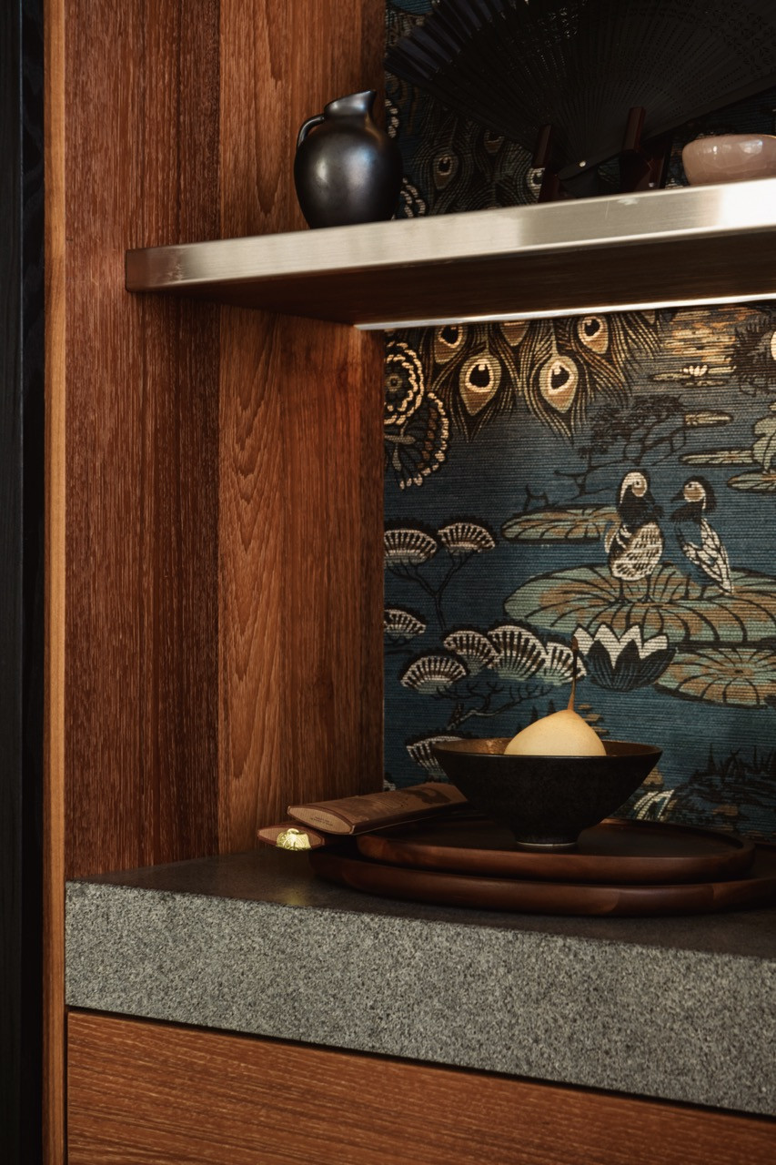 A detail of the custom display cabinet interior: warm walnut shelving lined with a peacock-motif fabric, a granite shelf, and a small collection of decorative objects