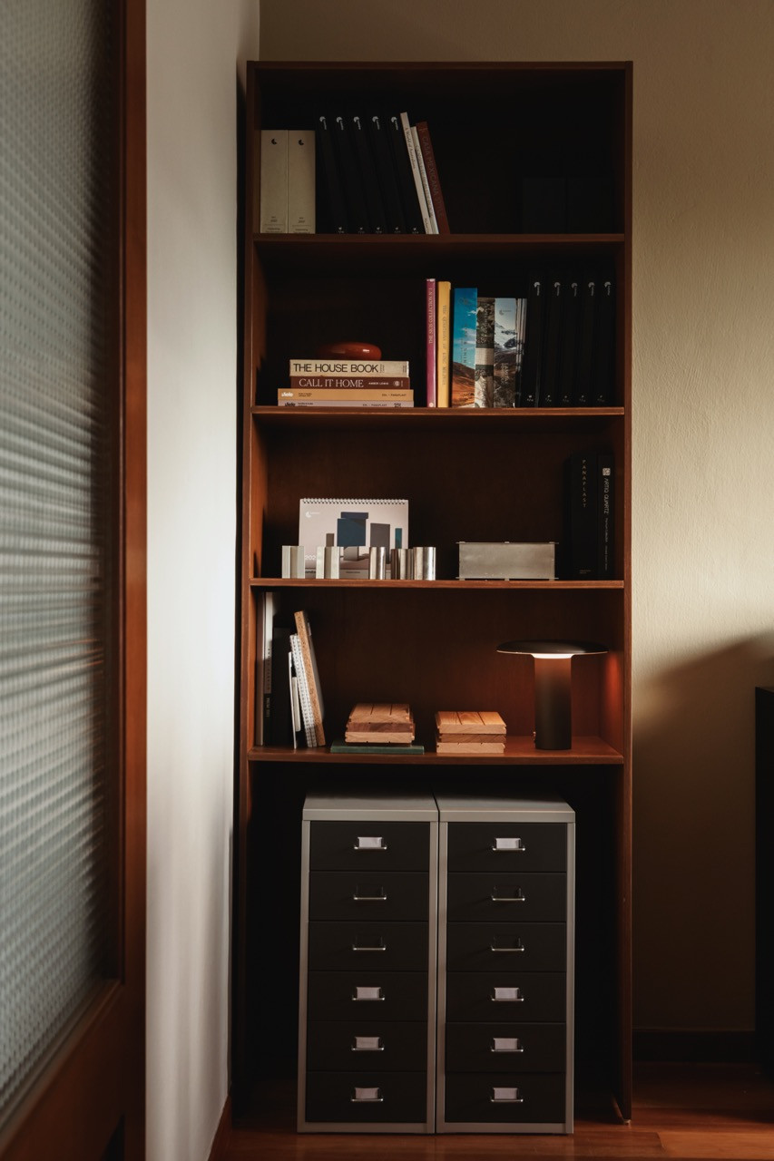 A walnut bookshelf holds design references and material samples alongside two metal filing cabinets