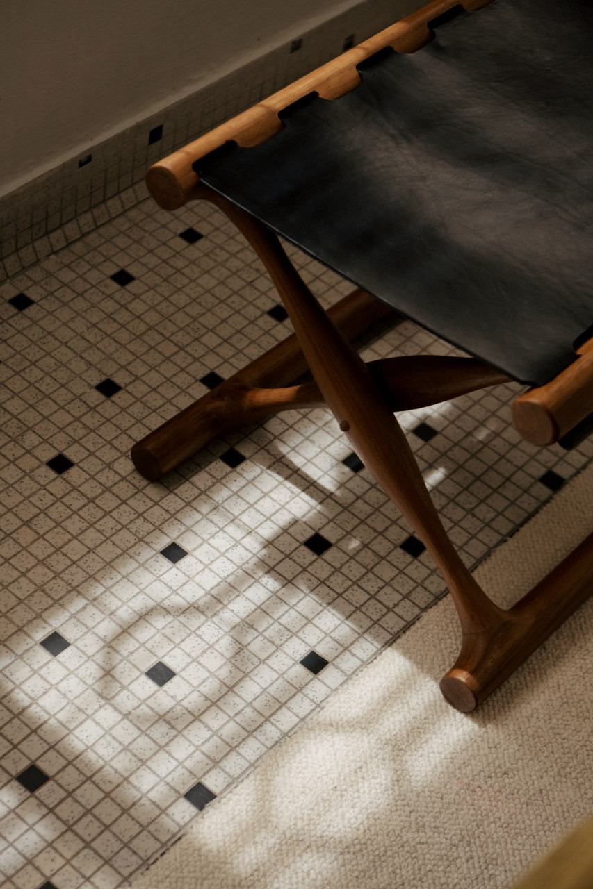 A detail of the original mosaic floor tiles, white with a black dot pattern, with the crossed teak legs of a campaign stool visible above
