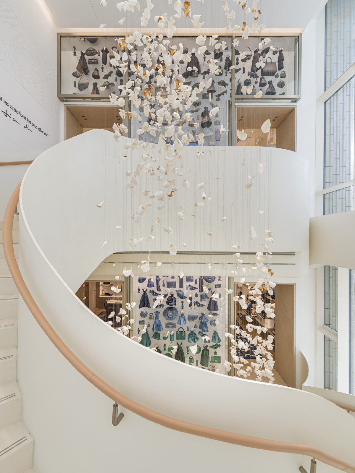 Viewed from the spiral staircase, a suspended installation of porcelain-like petals cascades through the atrium, framing display cases of Dior archive pieces on the floors below (Photo: Kristen Pelou)
