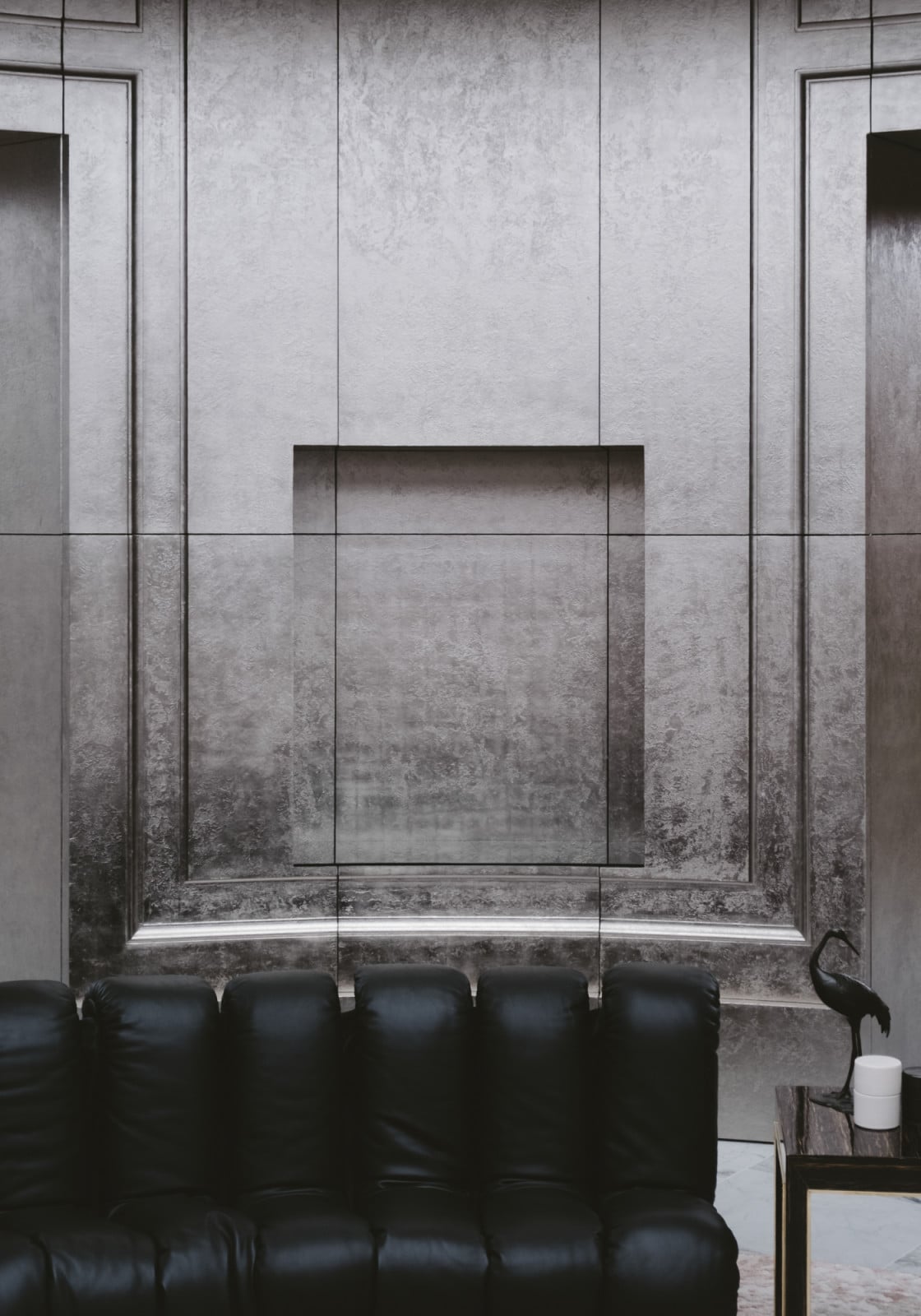 Textured plaster panelling frames a recessed niche above a leather banquette, its surface catching light across an uneven, hand-applied finish (Photo: Adagp)