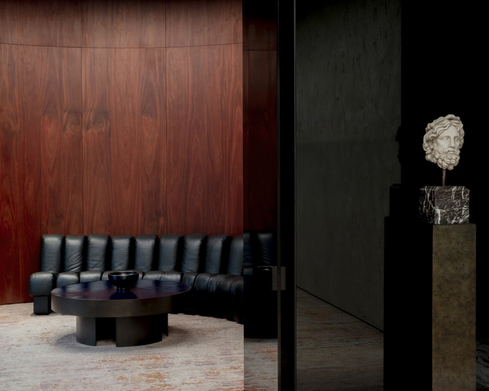 A curved wall in dark walnut panelling sets off a channel-tufted leather banquette and a low bronze table (Photo: Adagp)