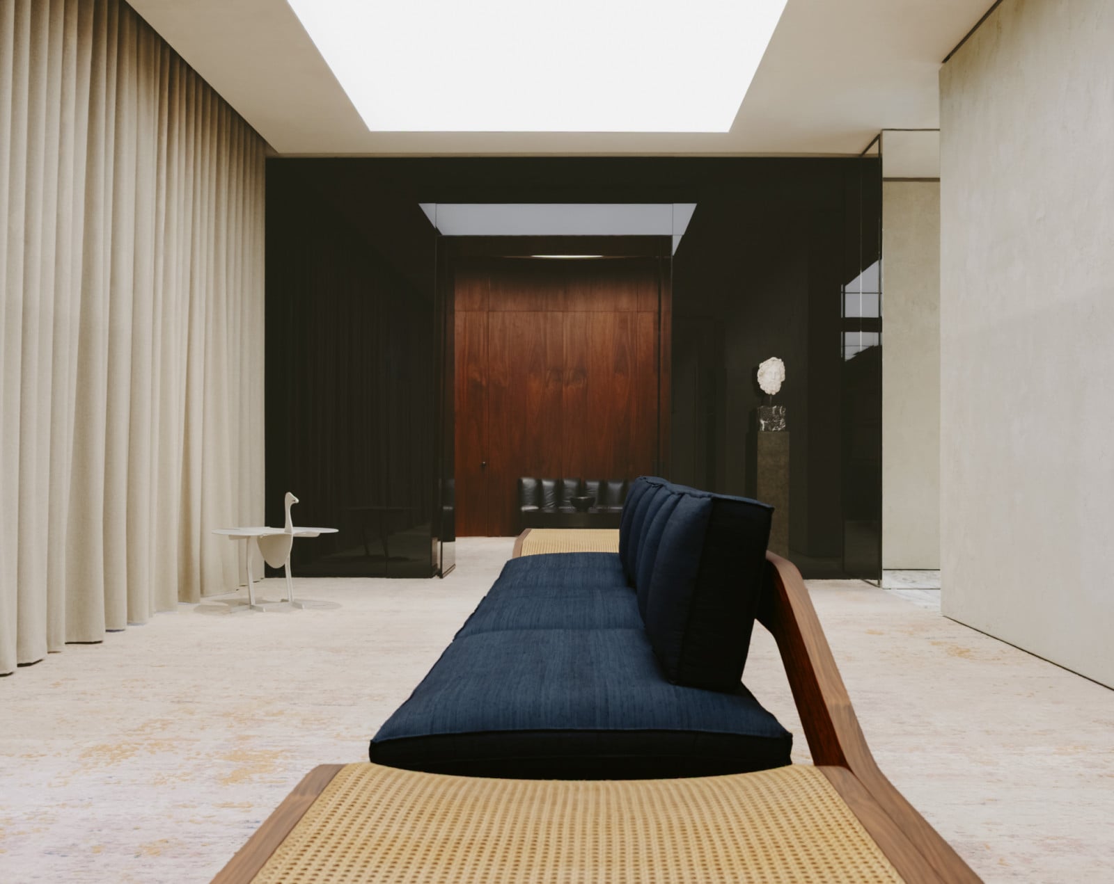 A daybed in cane and indigo linen sits at the centre of a room framed by heavy curtains and dark walnut doors (Photo: Adagp)