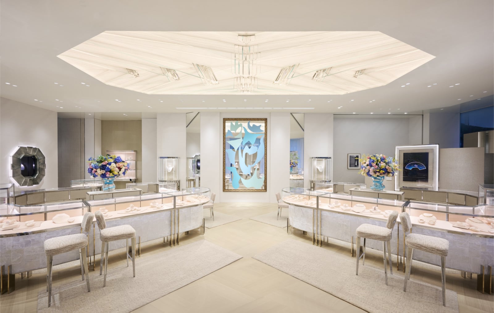 A jewellery salon is arranged around facing display counters in pale stone and bronze, with an angular pleated ceiling suspended overhead