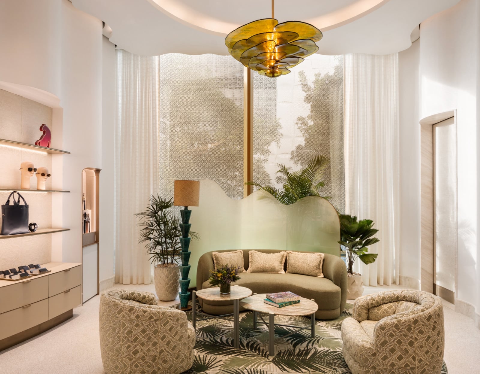 A private seating area is furnished with curved olive-toned sofas, set against sheer patterned curtains and a carved amber pendant light