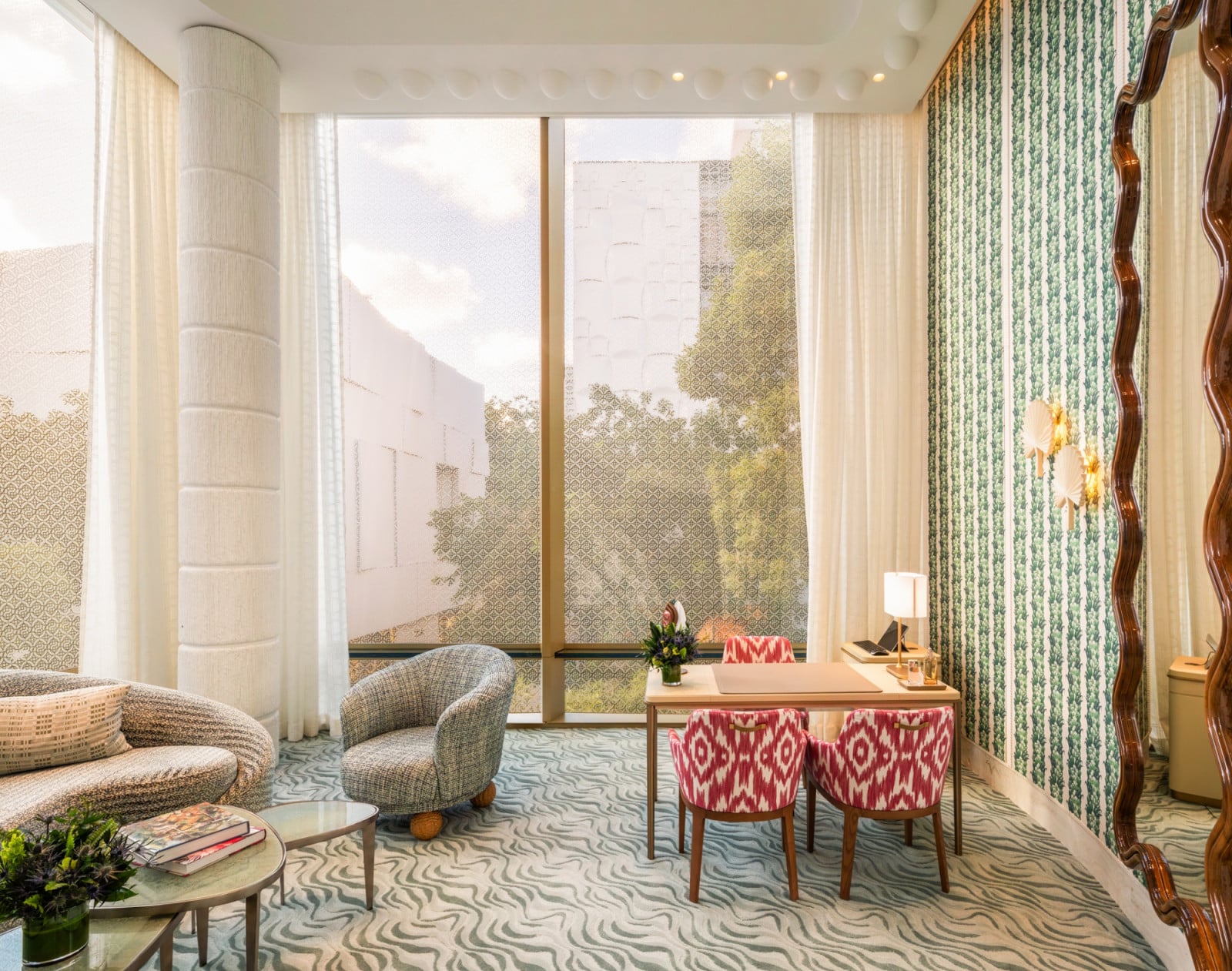 A lounge nook combines a textured column, striped green wallpaper and ikat-patterned dining chairs around a small desk