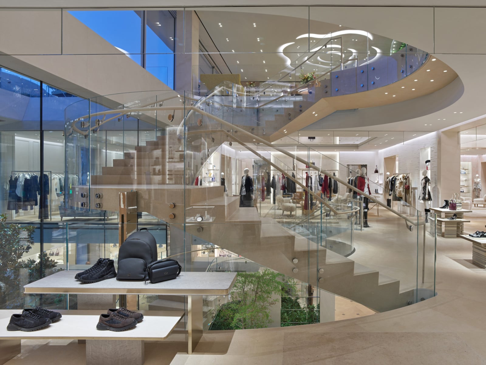 The store’s central staircase, in glass and pale stone, connects multiple levels beneath a rose-shaped light installation set into the ceiling (Photo: Jonathan Taylor)