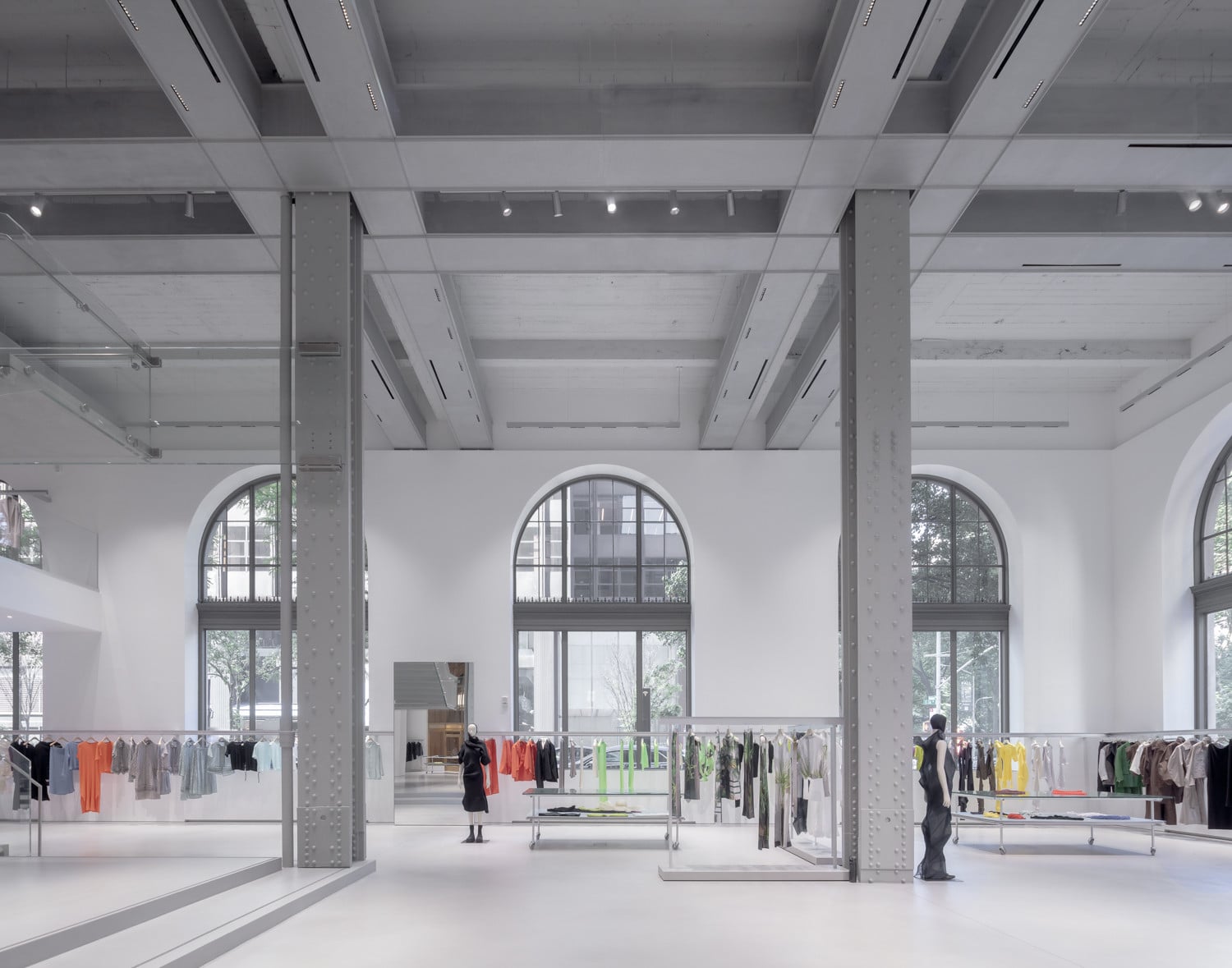 Clothing rails on wheeled glass stands sit beneath the original steel ceiling grid, positioned between three arched windows (Photo: Naho Kubota)