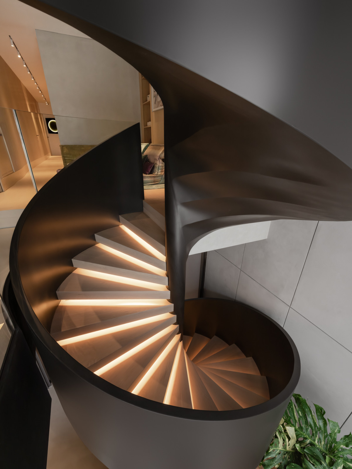 A close-up view of the rubber-oiled steel spiral staircase from the first floor, with the timber treads lit from below, looking down towards the children’s playroom