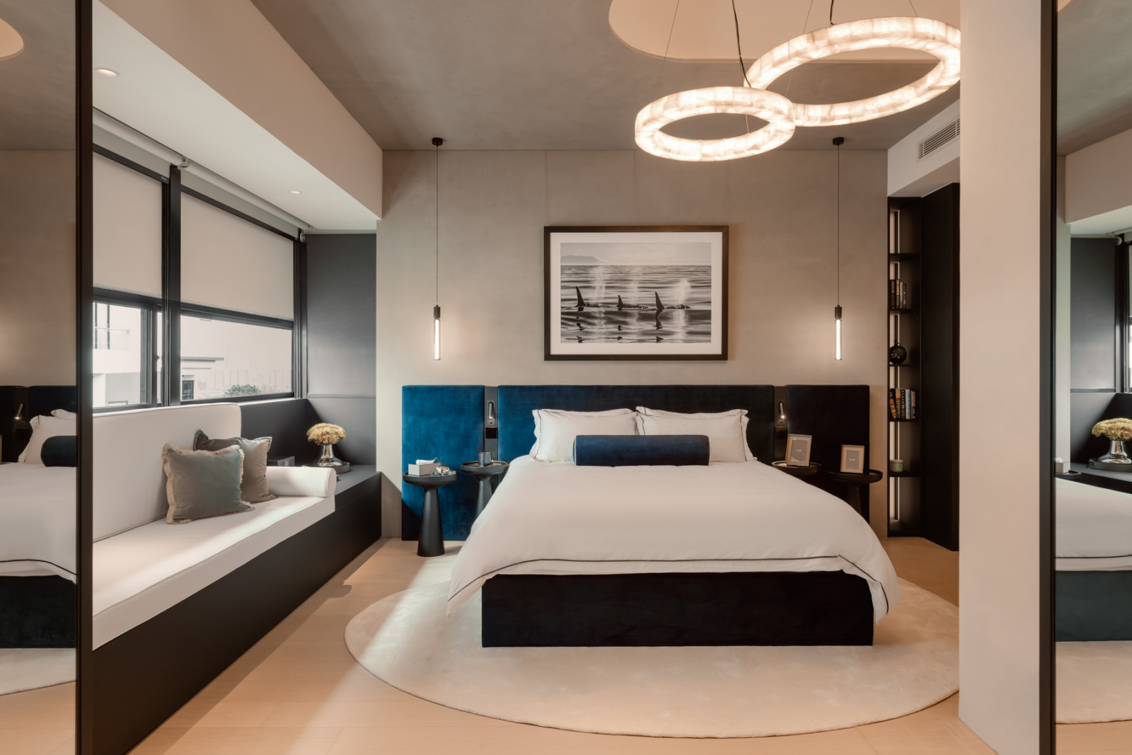 The master bedroom, governed by a near-monochromatic palette, features a deep blue velvet headboard, a halo pendant chandelier, and a window seat; the powder room, with the asymmetric Antonio Lupi basin set into a matte black vanity