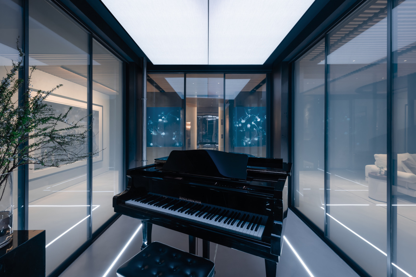 Inside the glass-enclosed piano room, the Rindlisbacher grand piano is framed by smart glass sliding doors on all sides, with the jellyfish tanks glowing in the foyer beyond