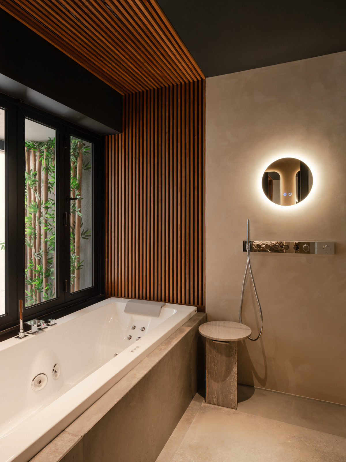 A master bathroom with a jacuzzi tub set, with a backlit circular mirror and Gessi fittings on the adjacent wall