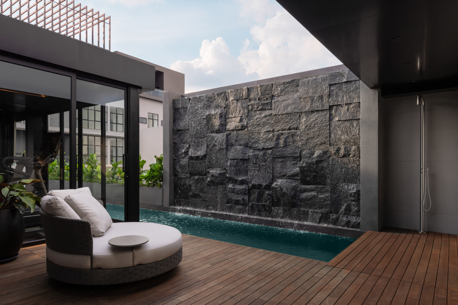 The rooftop pool terrace, with a circular daybed on a timber deck and a monumental rough-hewn stone feature wall