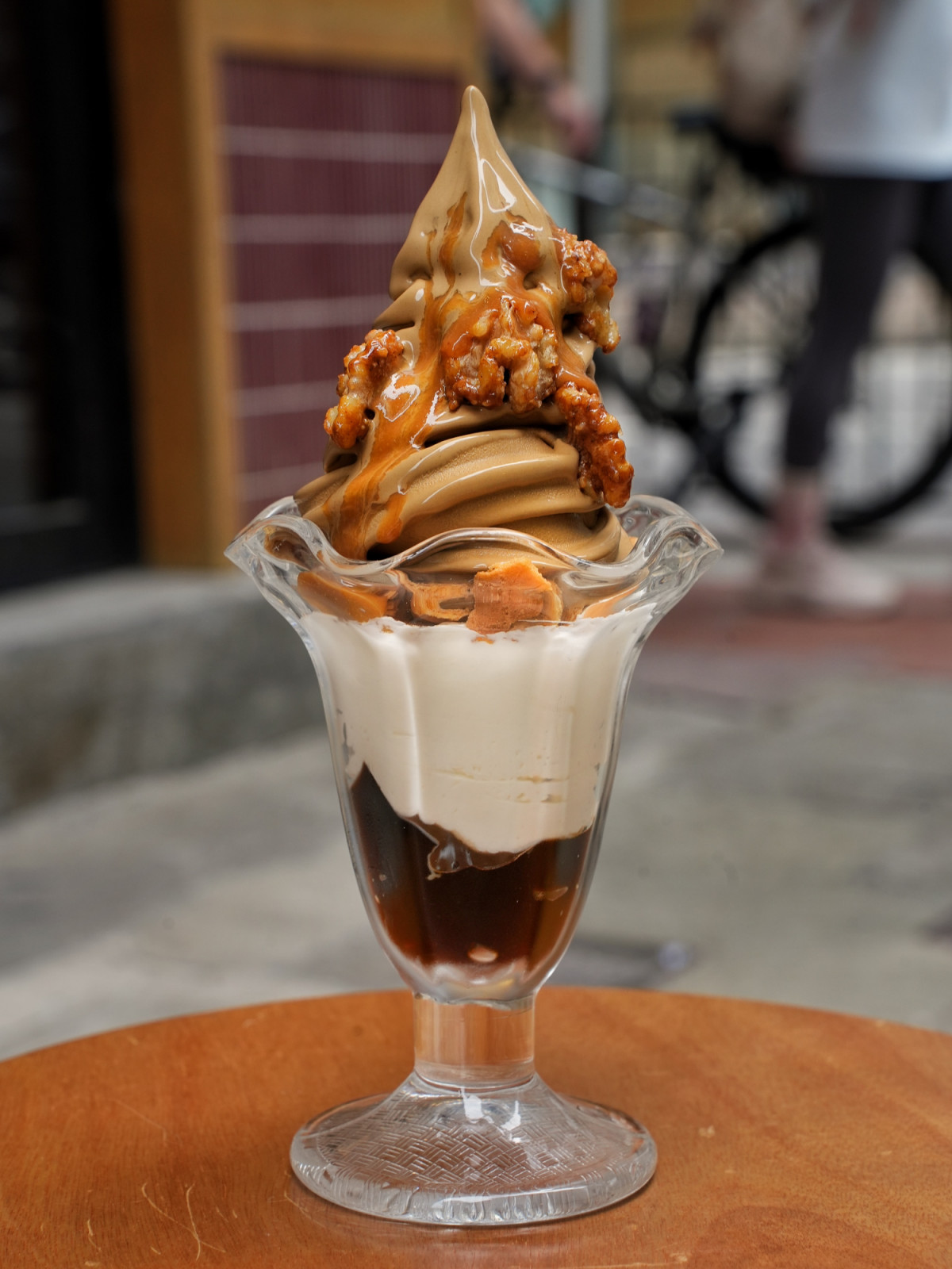 A towering parfait of rich soft serve ice cream from Via Tokyo, adorned with caramel-glazed nuts and layered with creamy sauces.