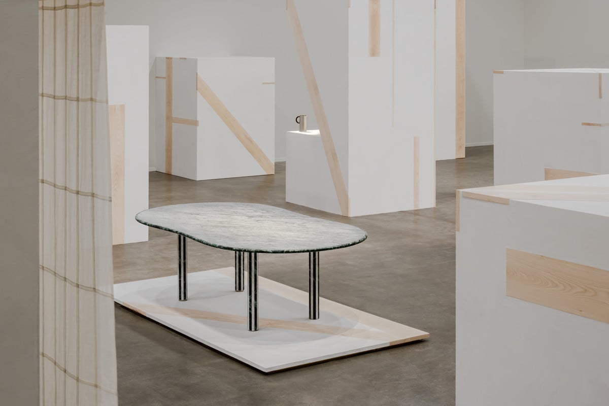 The H Letter throw prototype by Hyunjee Jung, crafted with bojagi technique, draped over a plaster box in the foreground of the Stadium d’Hermès table by Barber & Osgerby