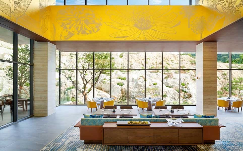 The resort’s restaurant, with floor-to-ceiling windows framing the granite rock face and a painted ceiling in yellow above the dining room (Photo: Oak Valley Resort)