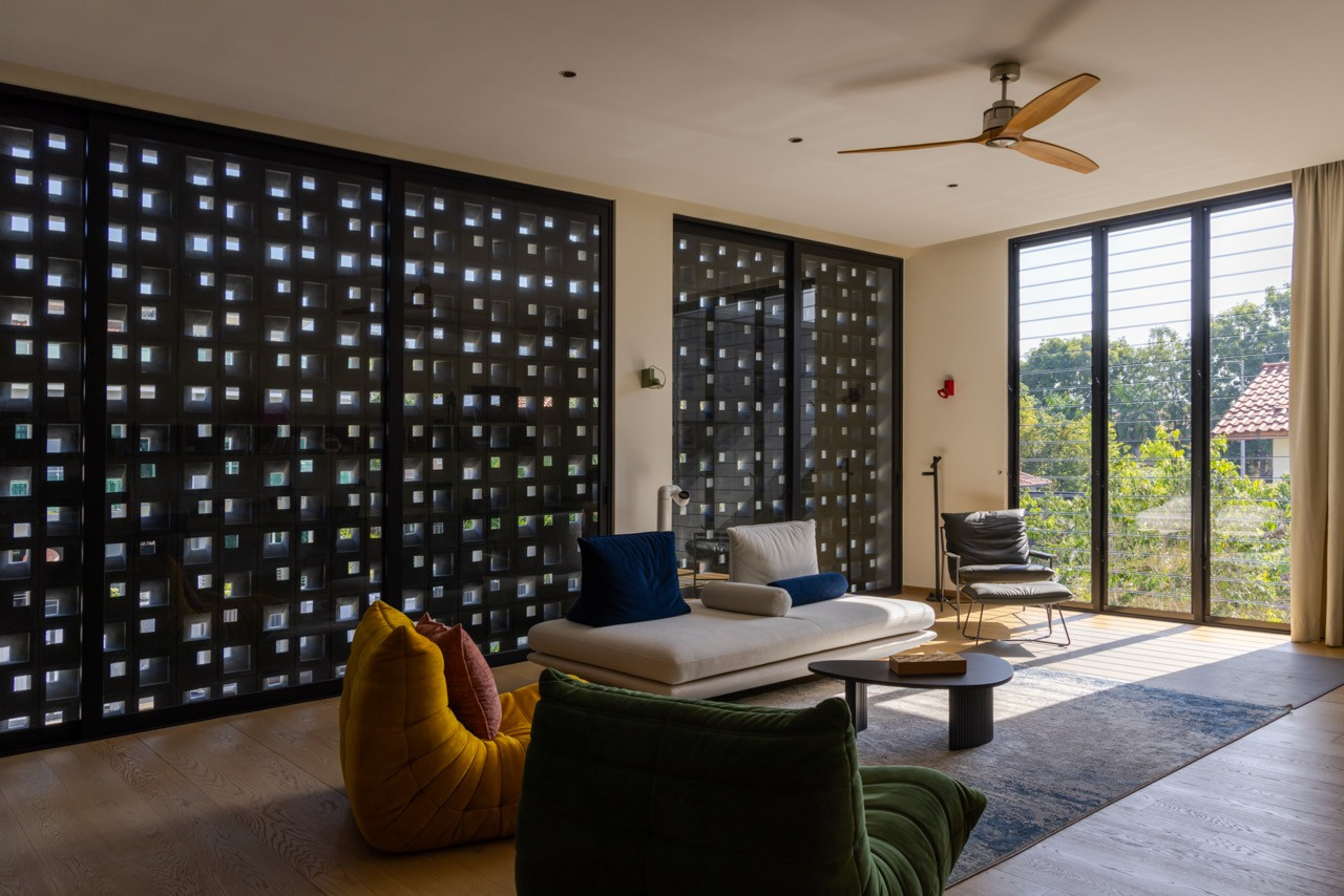 The concrete vent filters of the bedroom band line one wall of the family room, their pixelated pattern admitting filtered light while providing privacy and cross-ventilation