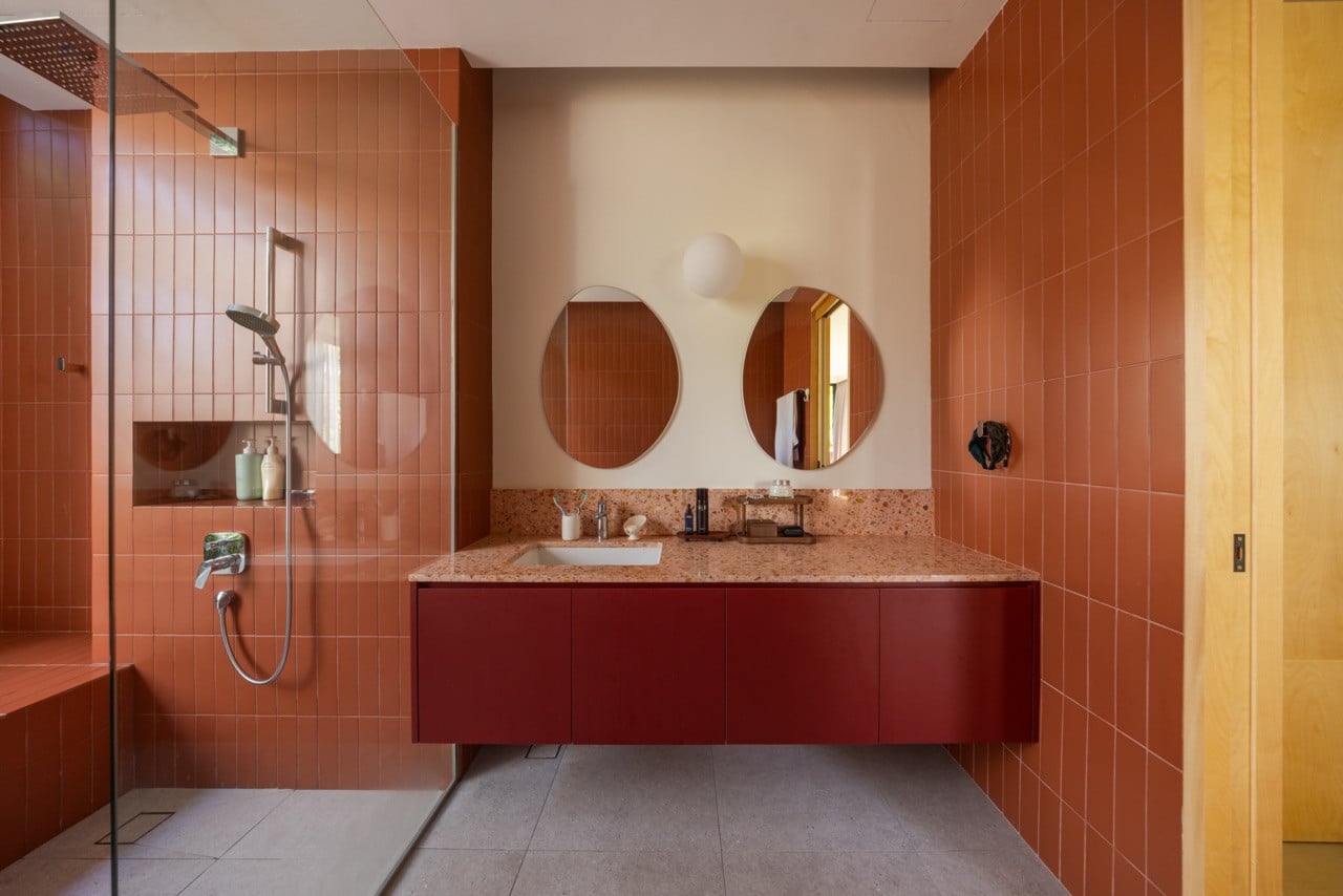 The master bathroom’s bathtub is set against an open garden court planted with aroids, with the grooved concrete of the exterior wall visible beyond the glass screen