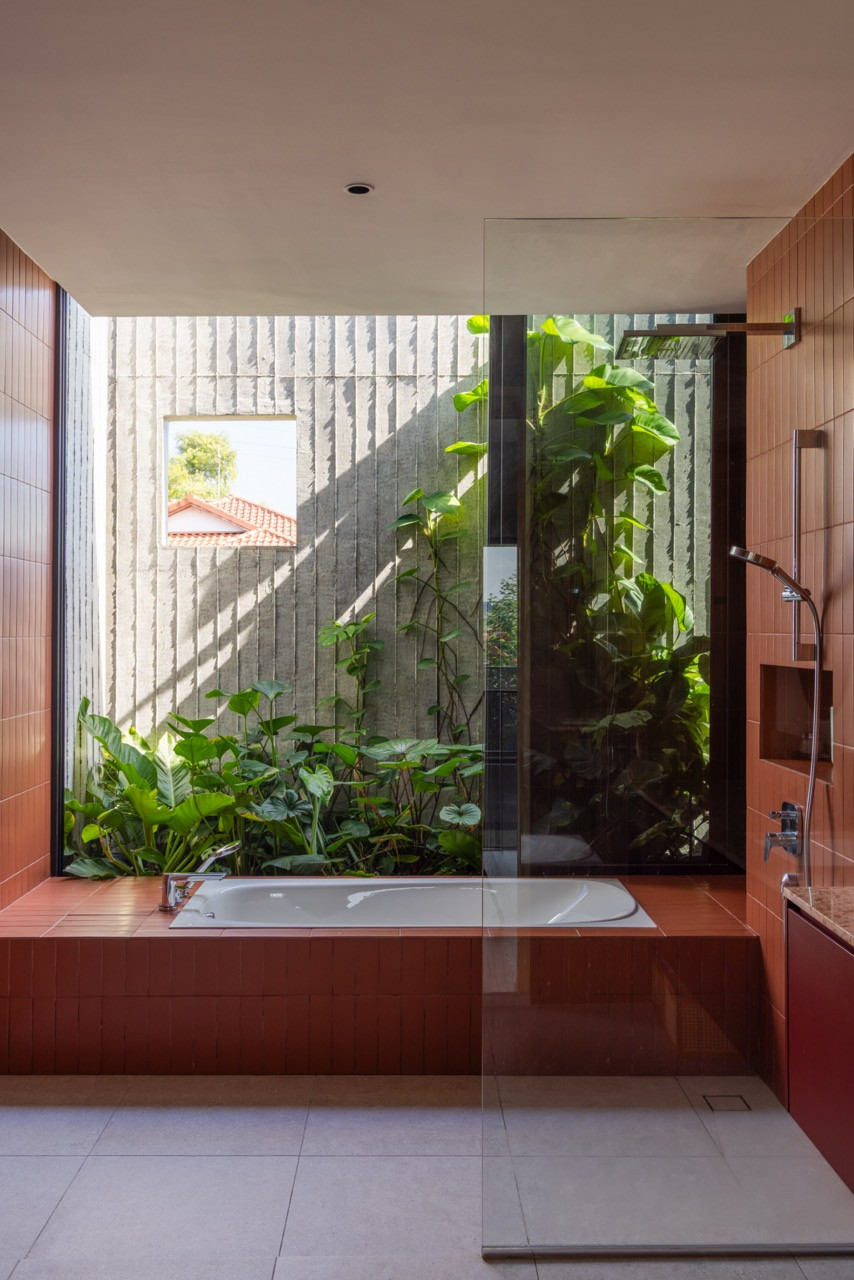 The master bathroom’s bathtub is set against an open garden court planted with aroids, with the grooved concrete of the exterior wall visible beyond the glass screen